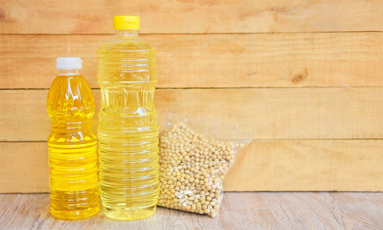 Bottles of soybean oil and bag of soybeans on a wood surface.