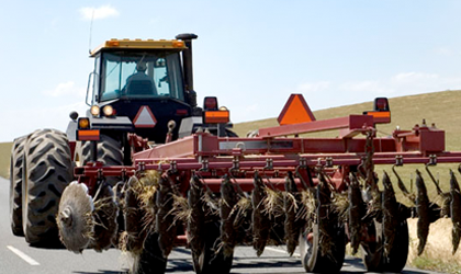 A red tractor driving on a county highway with an orange triangle sign on the rear.
