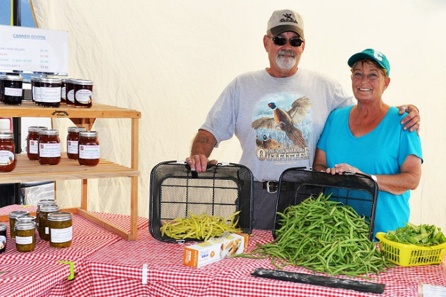 A husband and wife displaying fresh produce at a farmer's market stand.