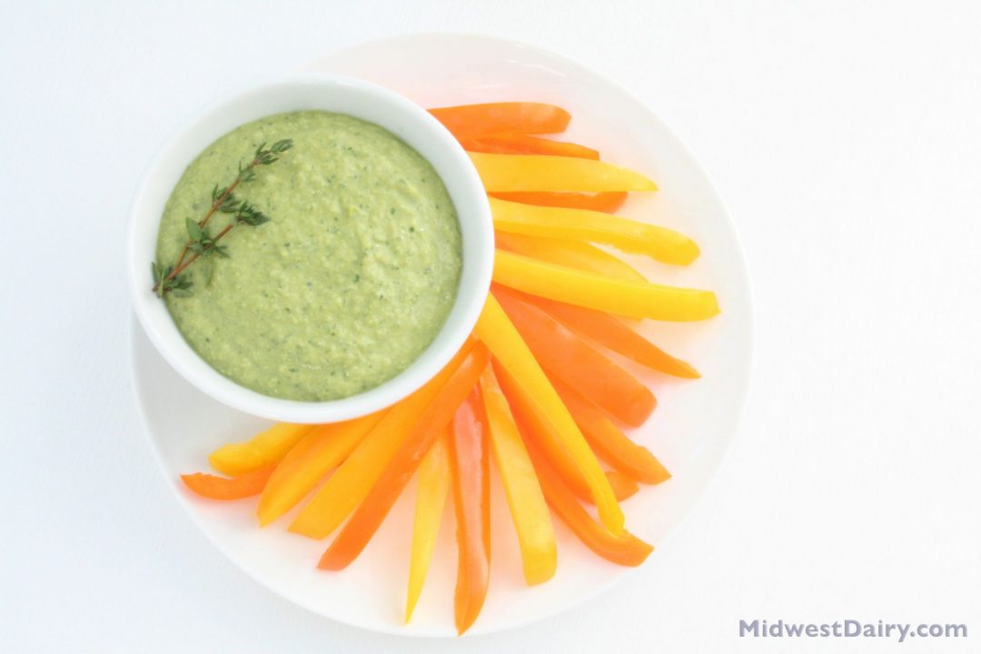 sliced orange and yellow peppers on a plate with green dip.