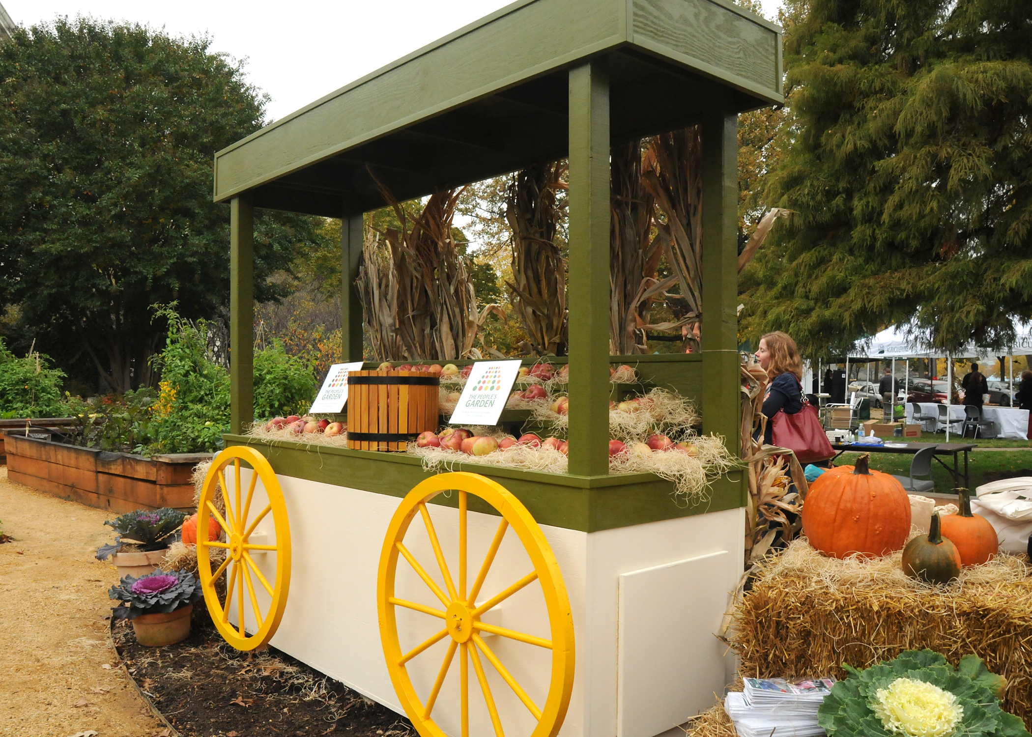 A produce stand with yellow wagon wheels and a green canopy.