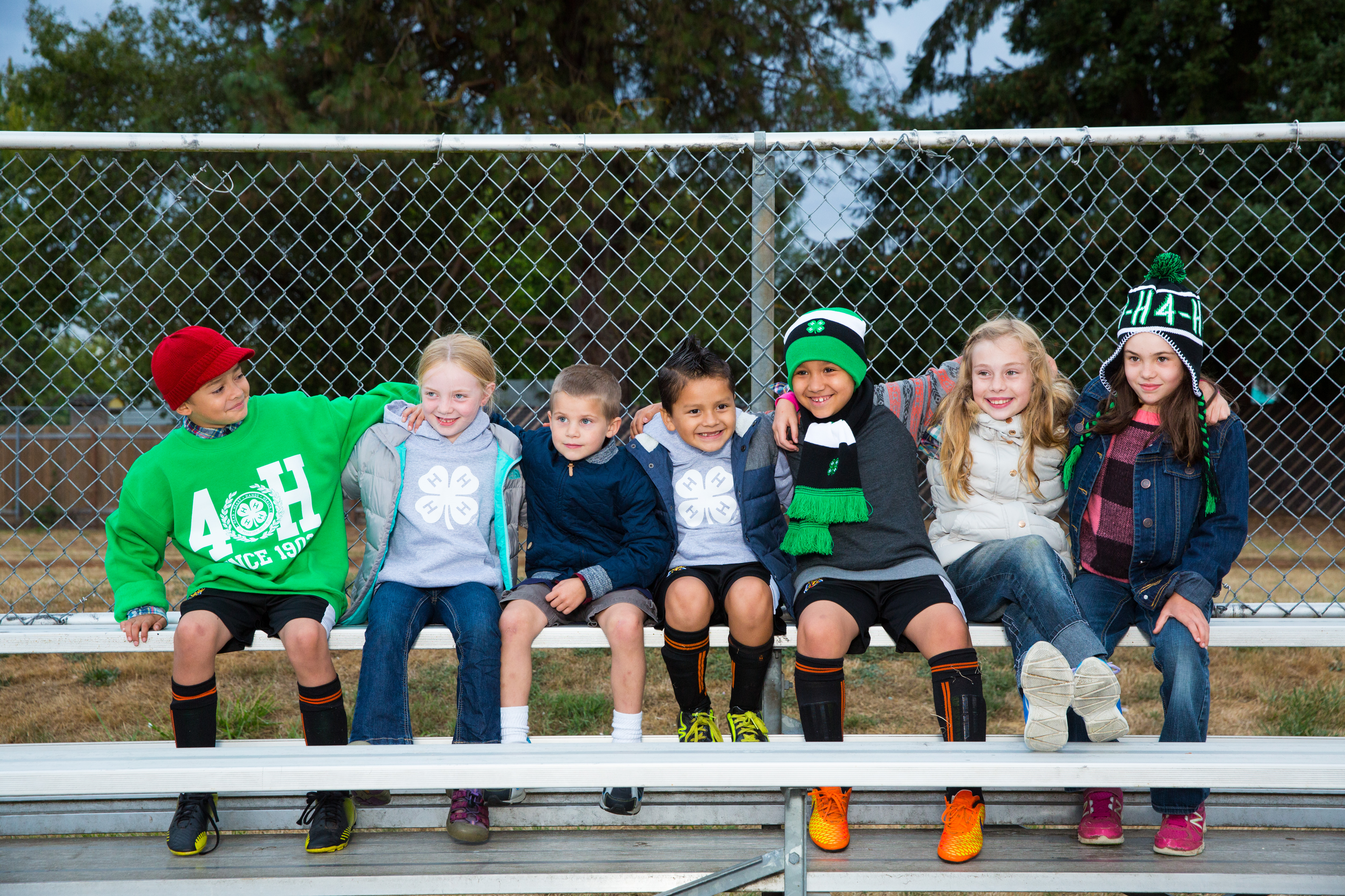 Diverse group of school-age children sitting on bleachers outside in 4-H clothing.; Photos; 4-H Grows Here; Brand; 4-H youth
