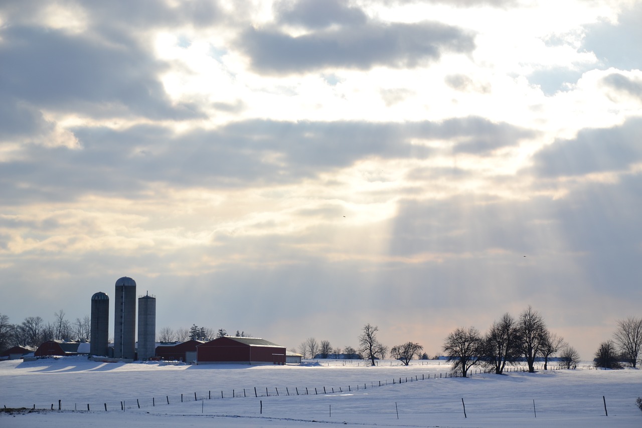 A snowy farmyard with sunlight breaking through the clouds.