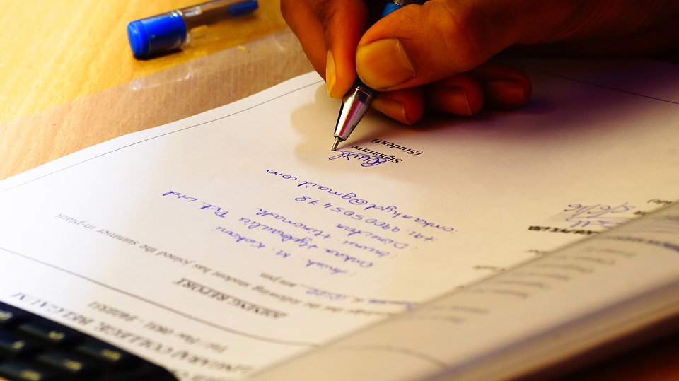 A hand writing on a financial document with a pen.
