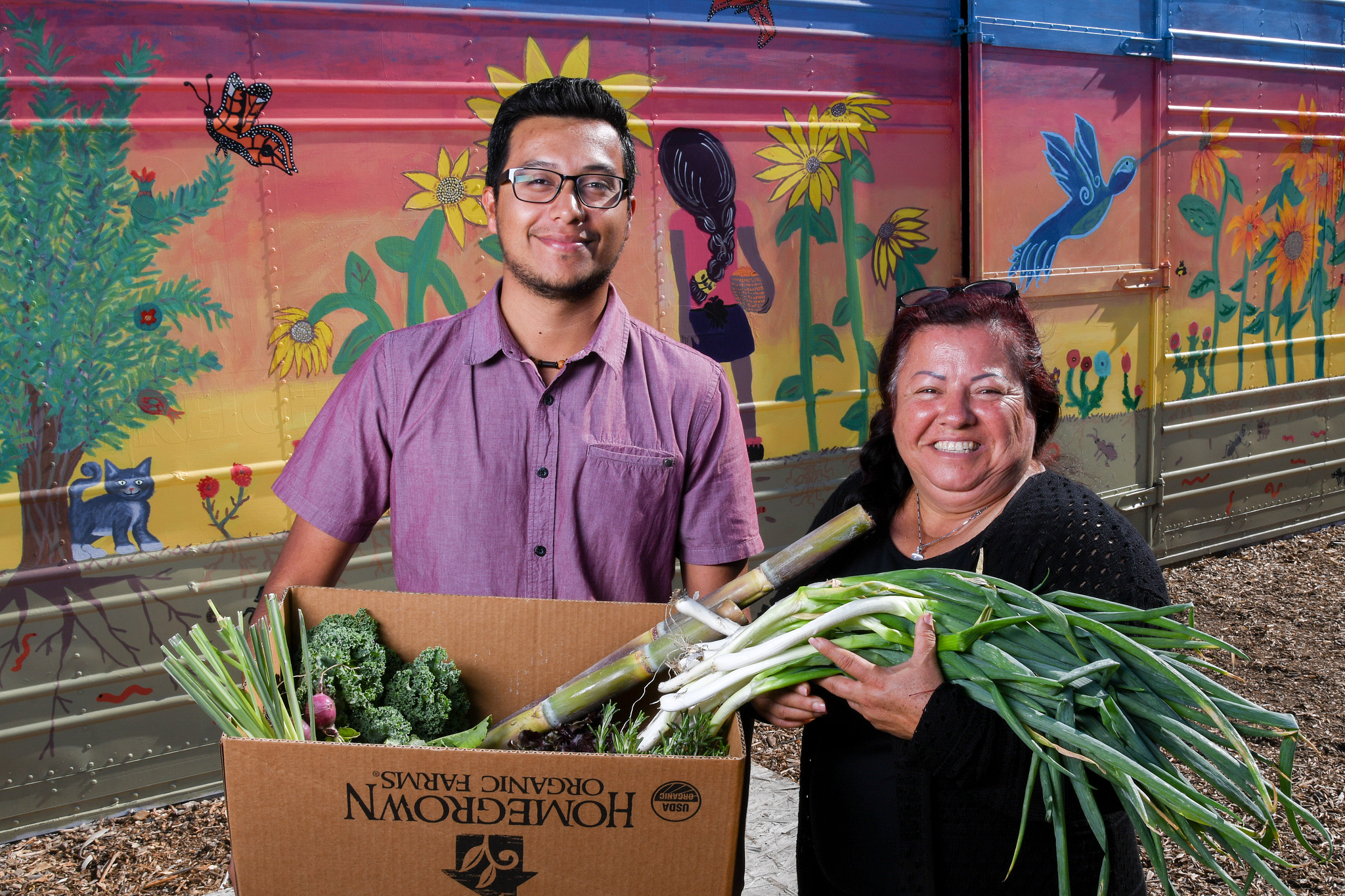 A young man and woman holding a csa box filled with fresh vegetables.