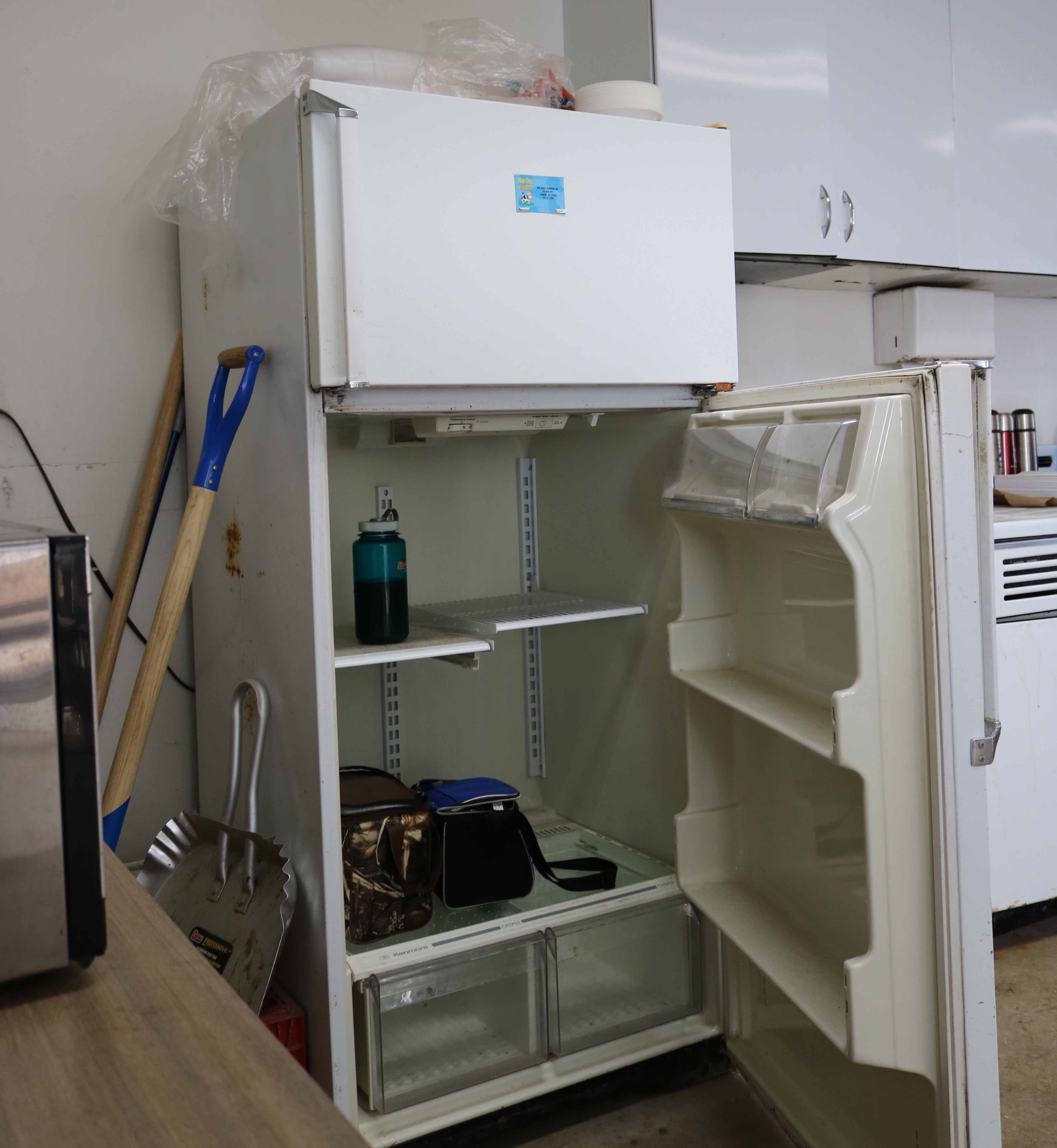 an white refrigerator with an open door. lunch pails and a bottled beverage are inside. a sink and kitchen area are next to it.