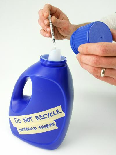 Hand depositing needle in blue detergent bottle labeled "do not recycle. household sharps."