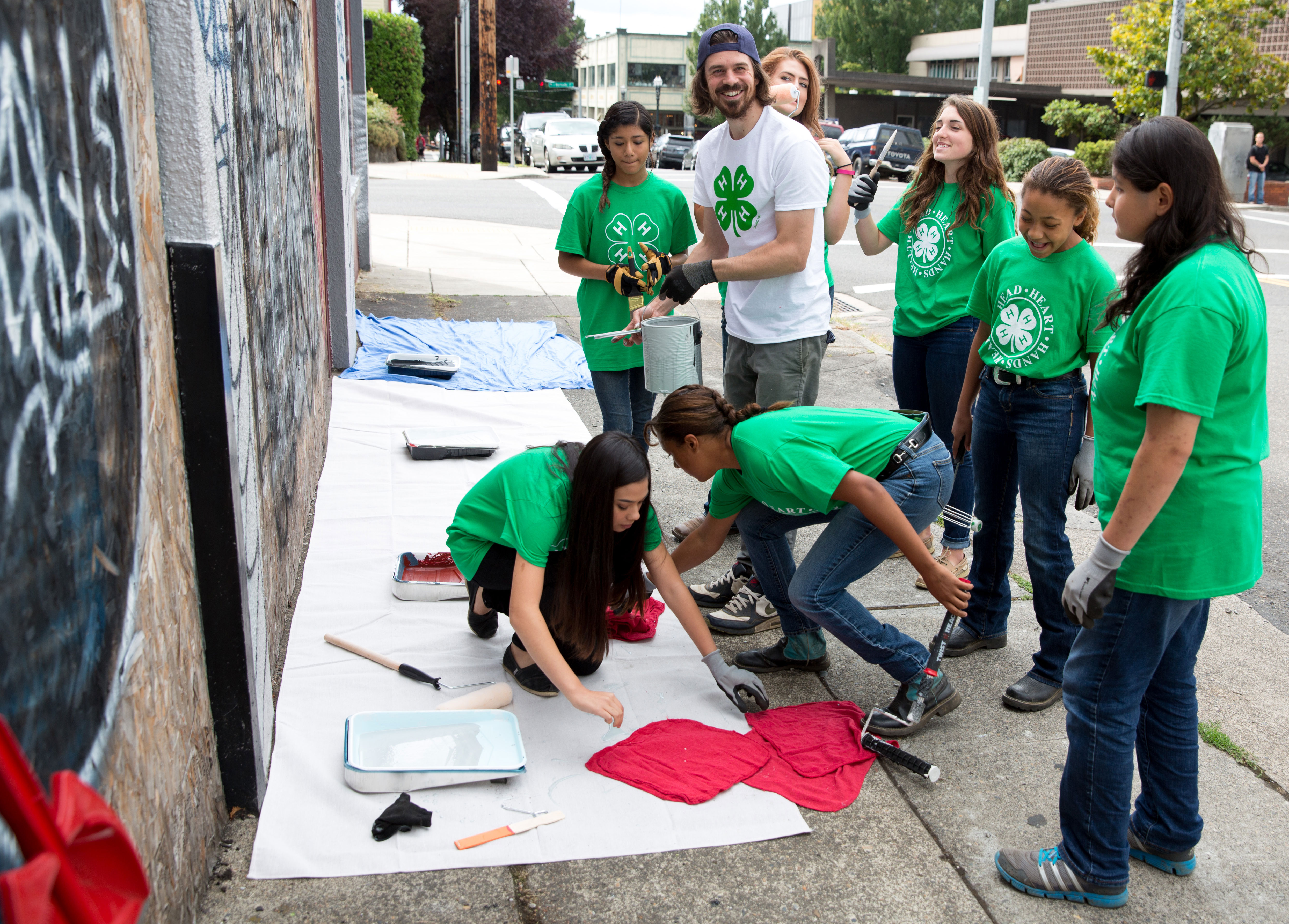 a small group of 4-H youth painting over graffiti with their 4-H youth advisor. Photo courtesy of National 4-H.