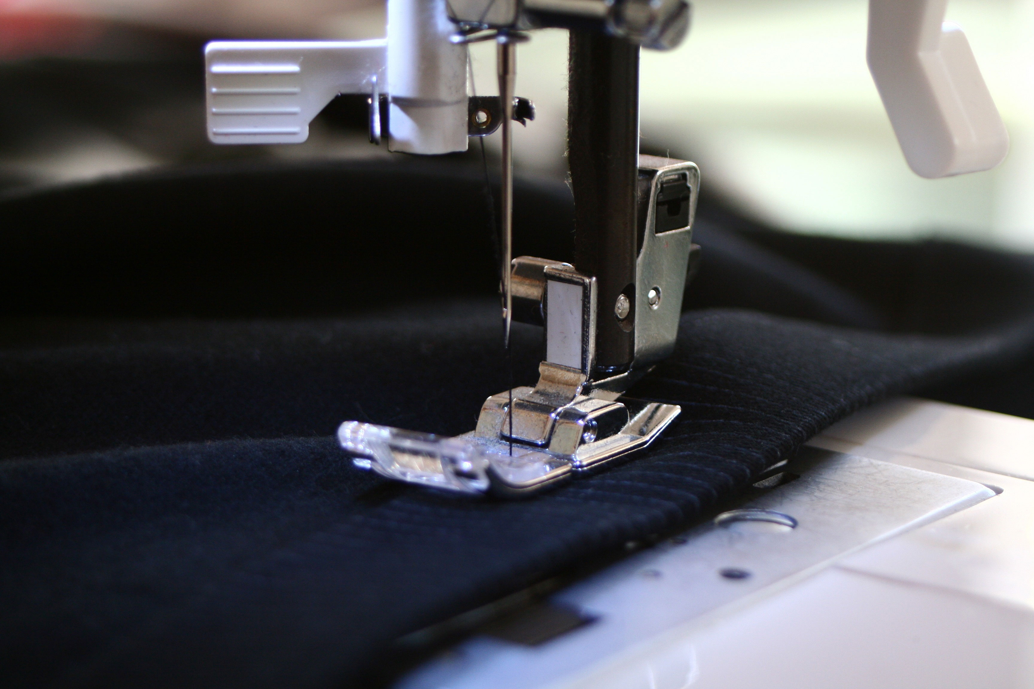 a sewing machine stitching a piece of navy blue fabric
