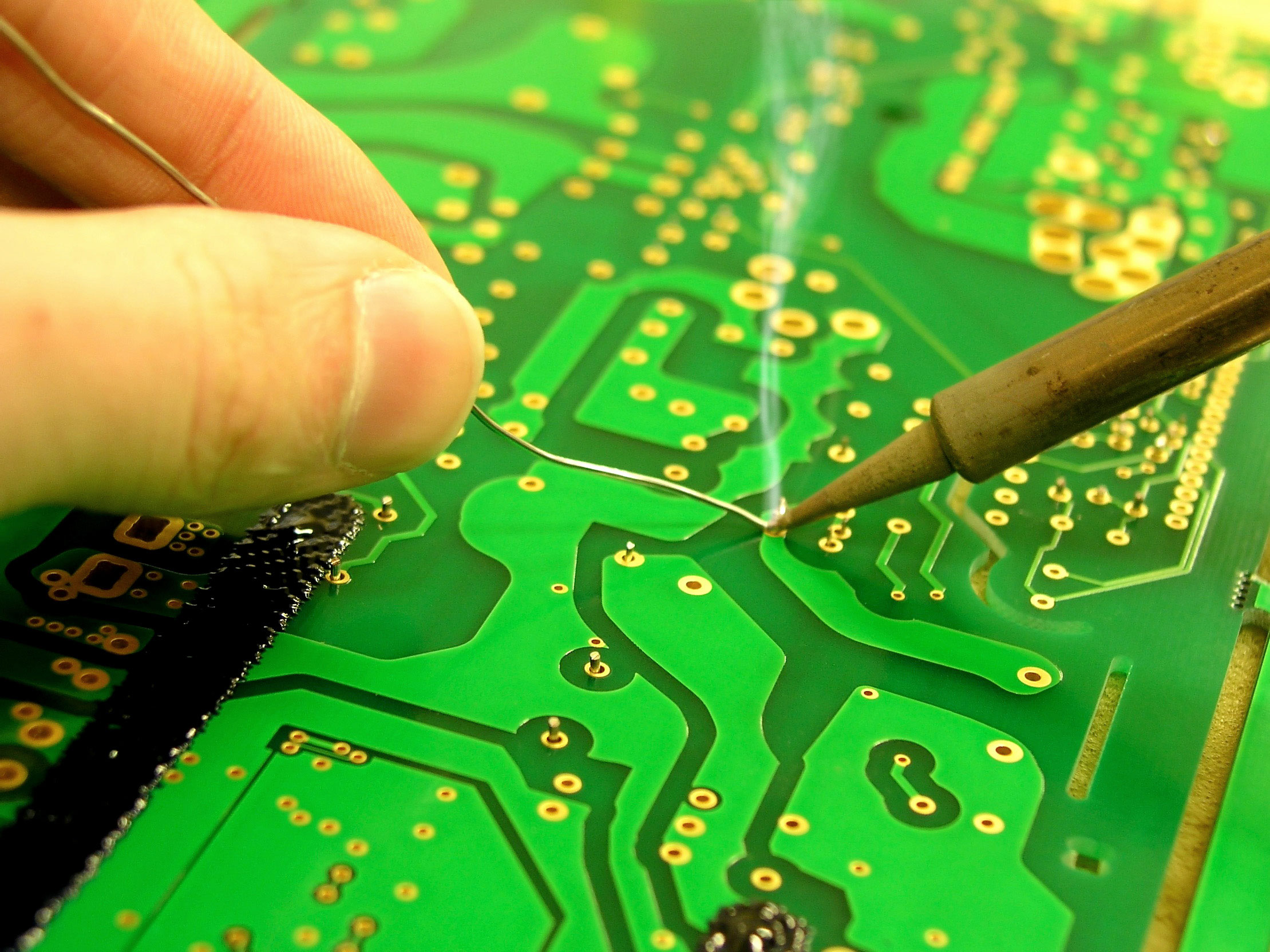 pair of hands soldering a green electronic circuit board