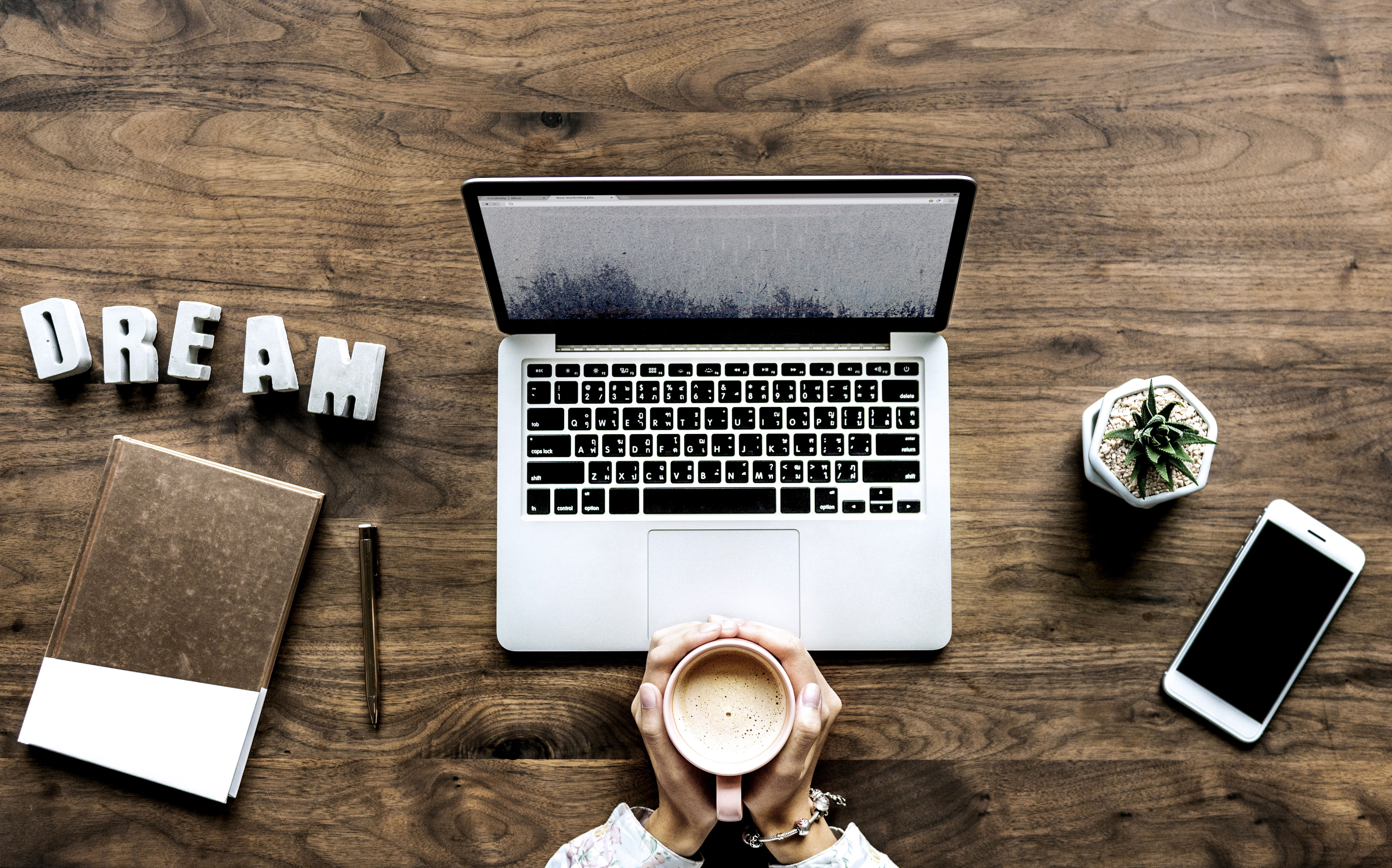 laptop, cell phone, and notebook sitting atop a brown, wooden desk.