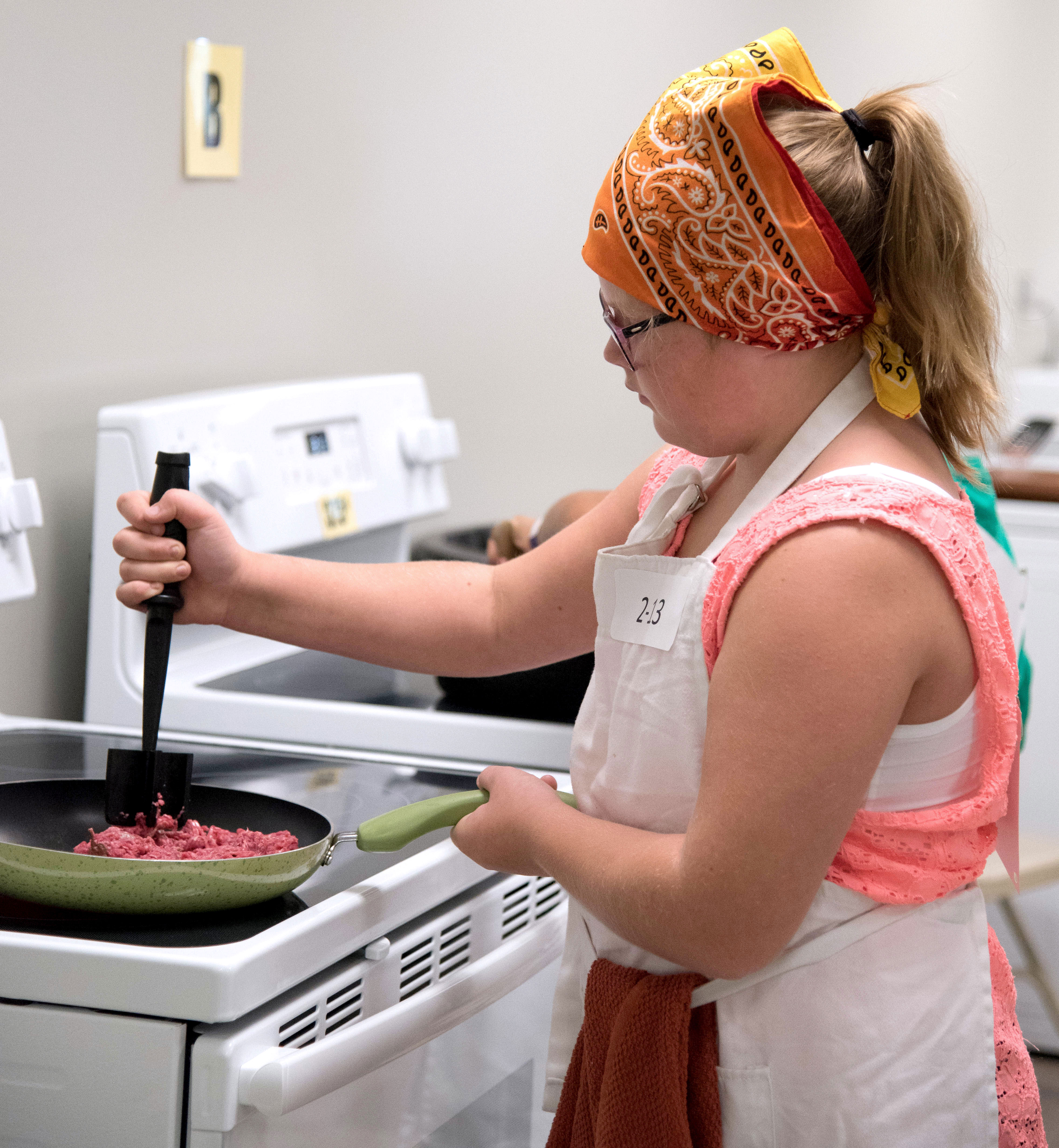 female youth cooking ground beef in a frying pan