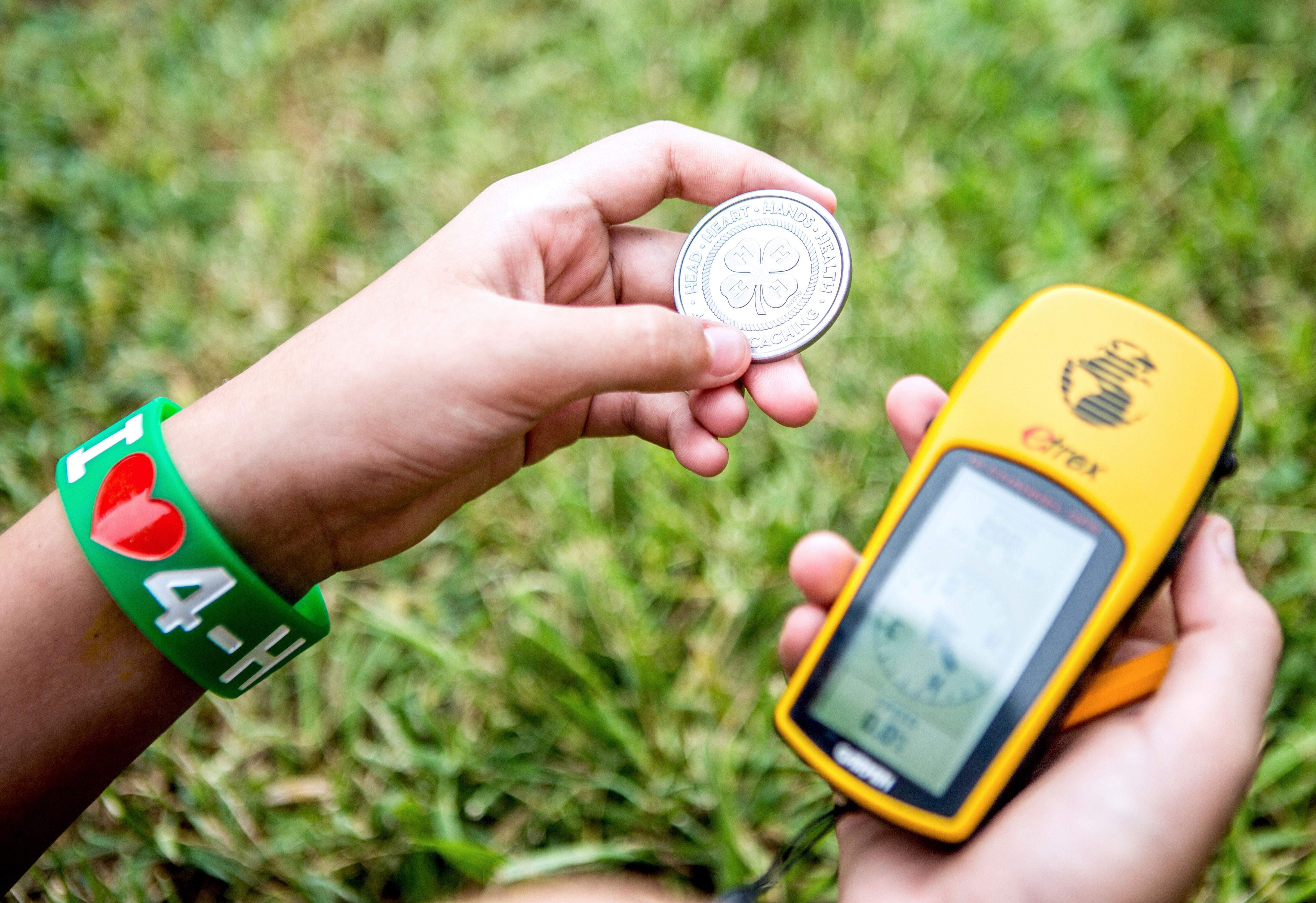 hands holding a 4-H coin and a gps navigational device