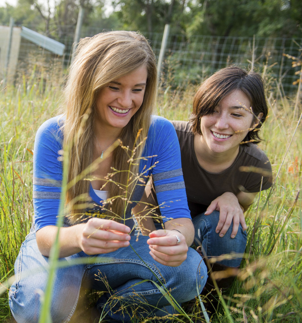 two female youth inspecting a plant in a pasture