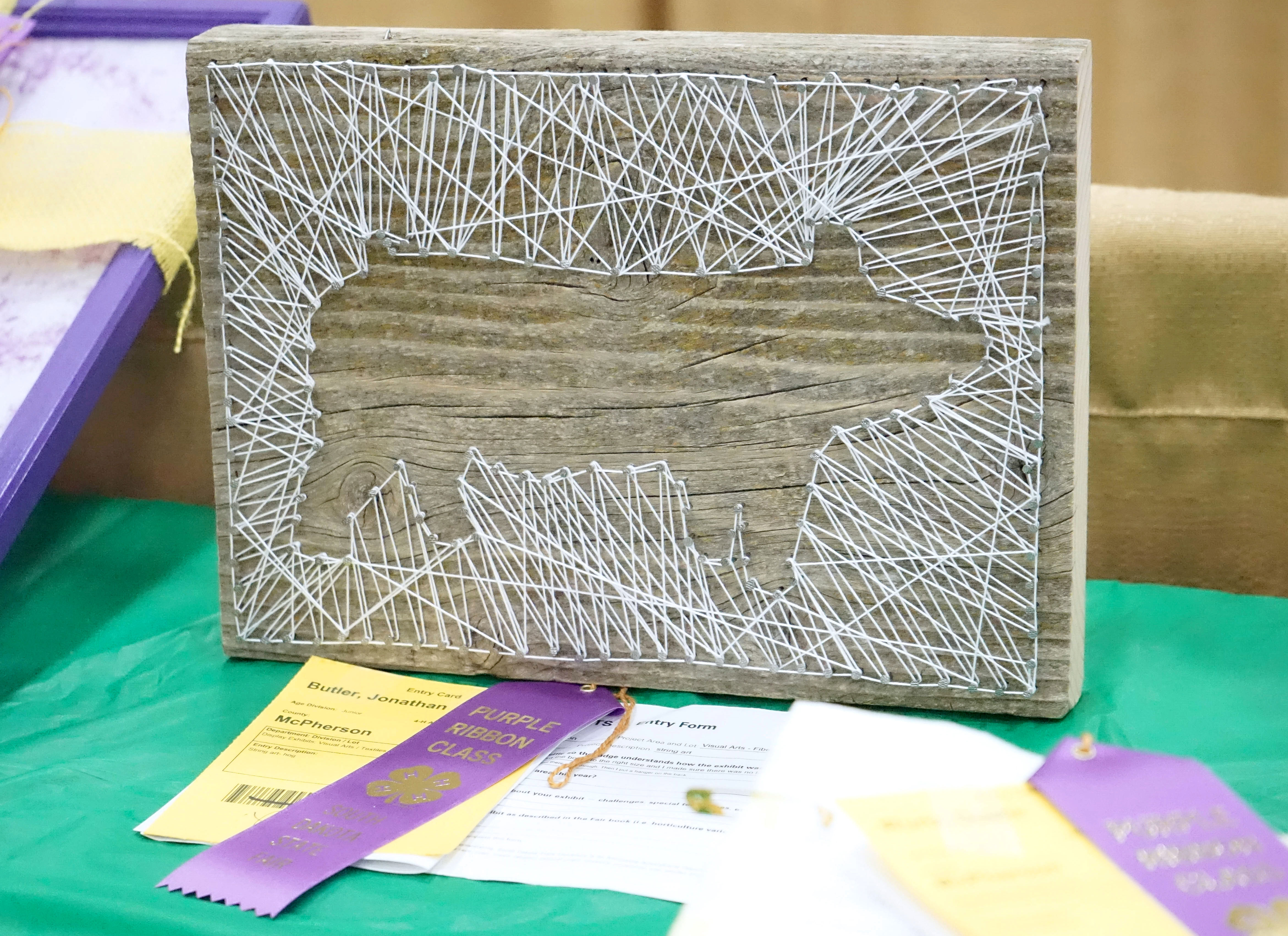 Silhouette of a pig on a board wrapped in white twine. two purple ribbons on the table next to it.