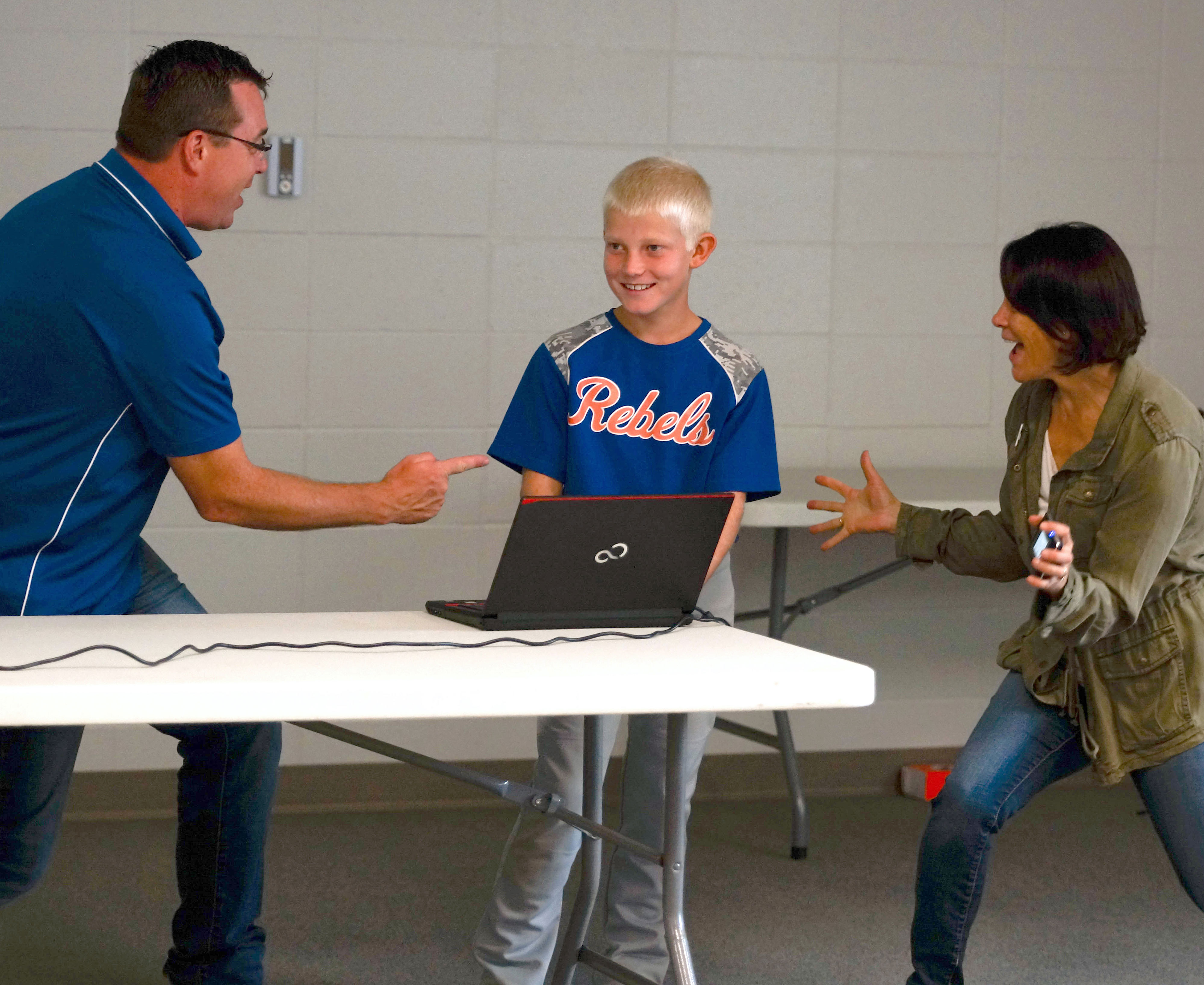 male 4-h youth in a baseball uniform standing between an adult male and female during a presentation