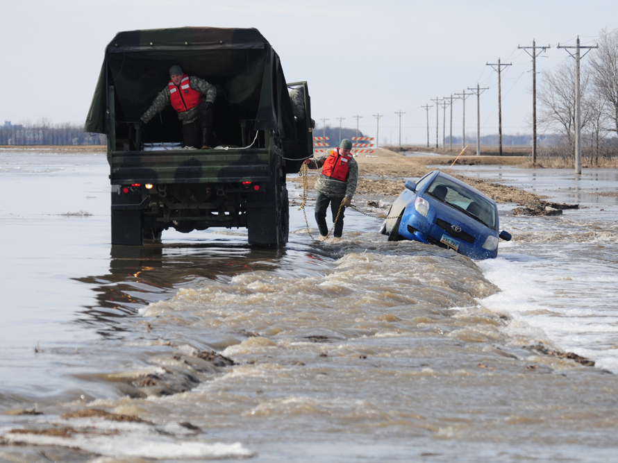 A car being towed a flooded, washed out gravel road by a national guard truck. Photo by Senior Master Sgt. David H. Lipp, U.S. Department of Defense