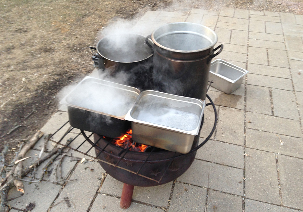 a small fire kettle with several pans of boiling sap atop its grill
