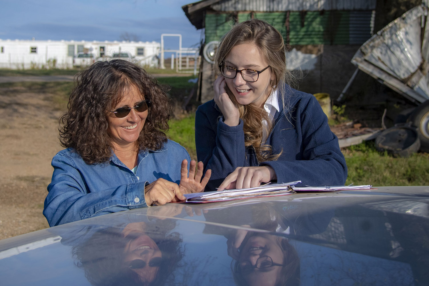 two female ag workers smiling while reviewing a document on the hood of a pickup