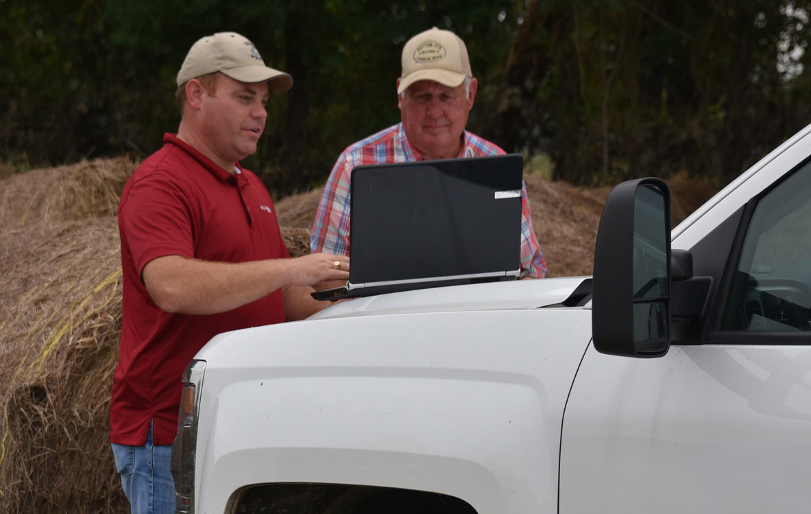 two men viewing a laptop on the hood of a white pickup