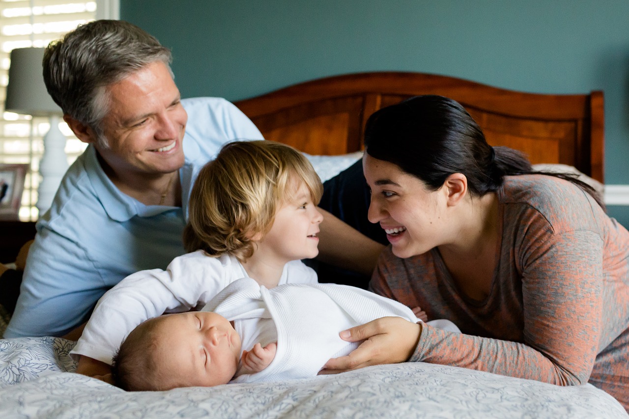 a happy mother, father, son, and newborn together on a bed.