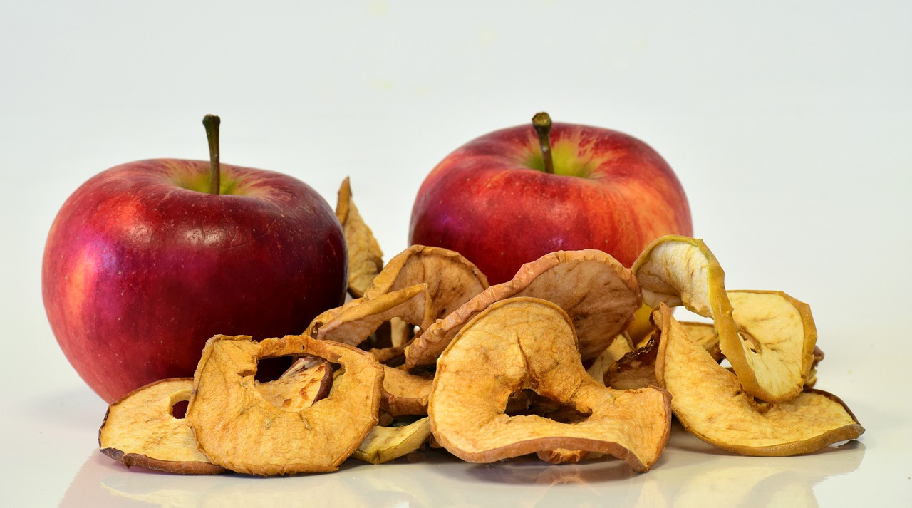 two whole apples behind a small pile of dehydrated apple slices