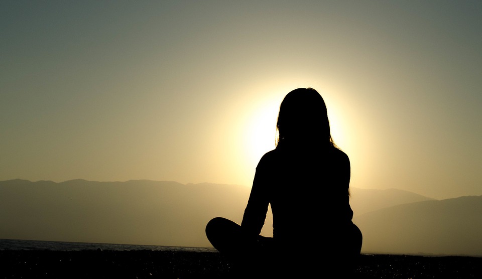 silhouette of a woman meditating. sunset in the background.