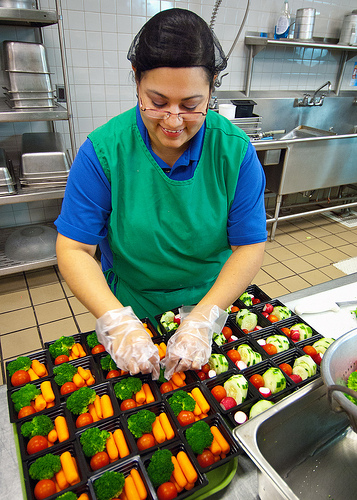woman wearing gloves preparing servings of vegetables. USDA Photo Courtesy of Bob Nichols.