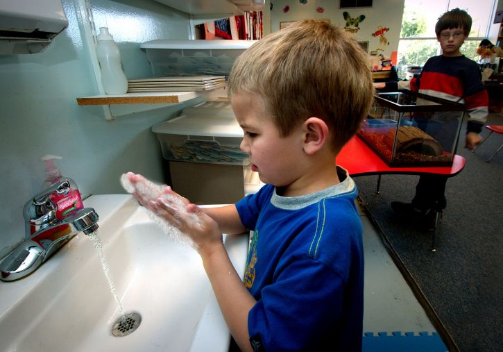 young boy washing hands at a sink in a classroom.