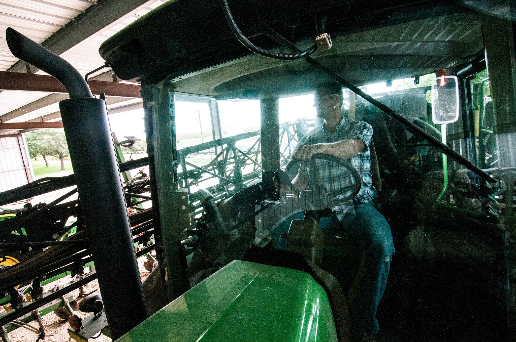 Farmer sitting inside the cab of a green tractor parked inside a machine shed.