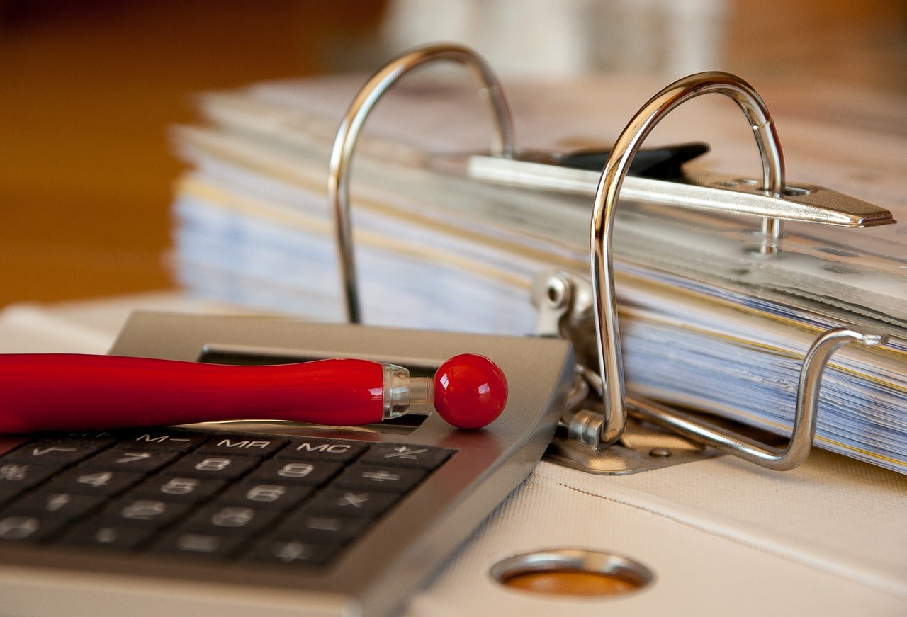 A pen and calculator sitting next to an accounting binder.