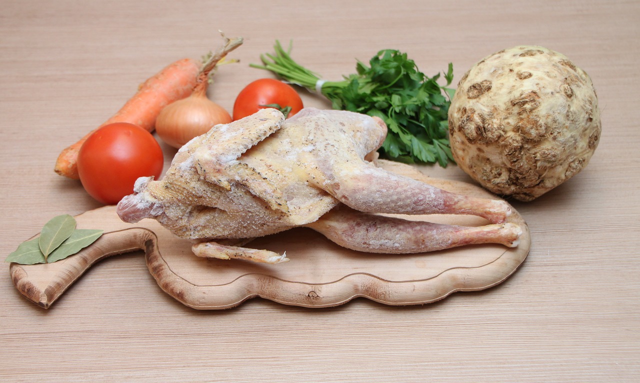 An uncooked, seasoned whole chicken on a cutting board with fresh vegetables.