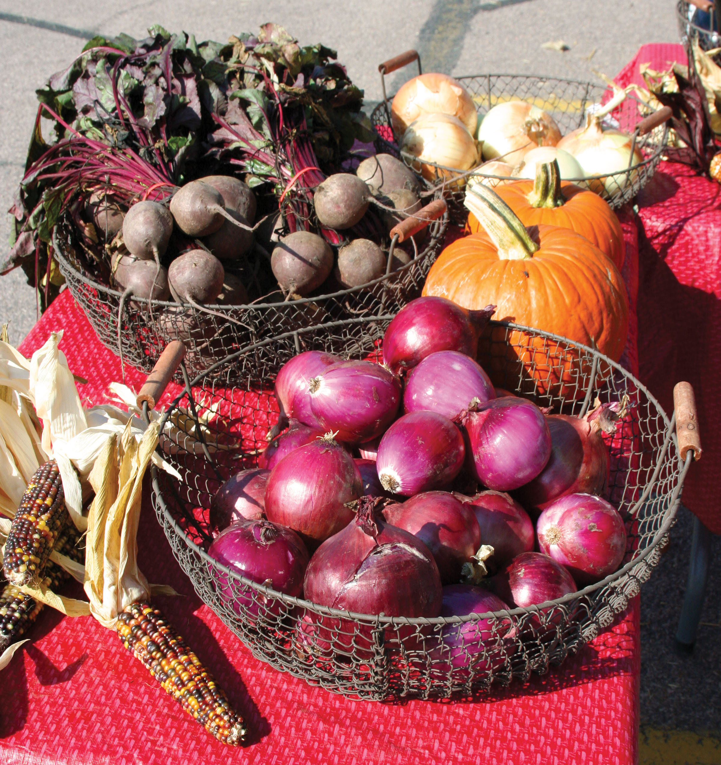 Indian corn, onions, pumpkins, and beets displayed on a table at a farmers market.