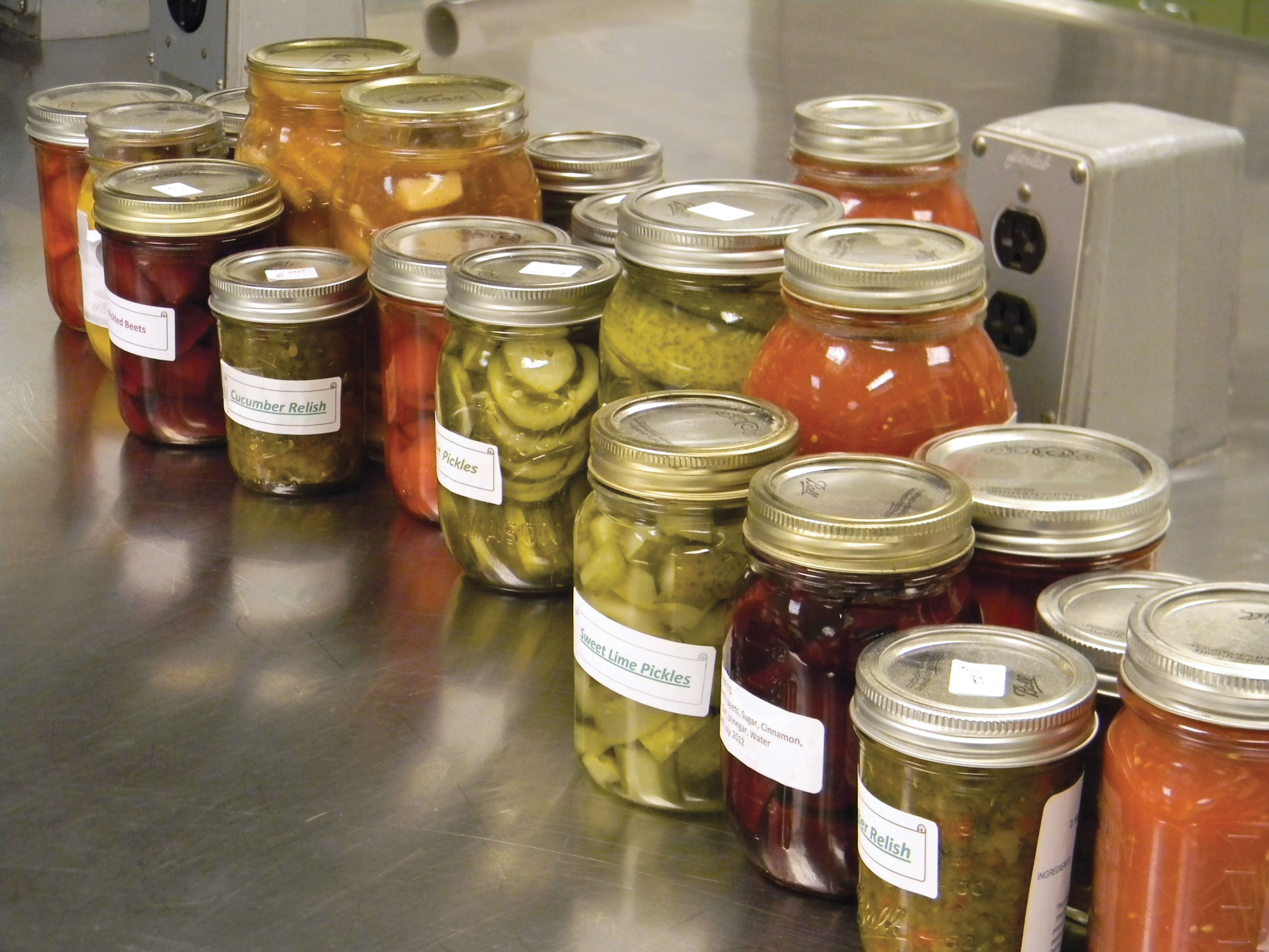 Variety of home-canned, pickled vegetables on a silver table in a kitchen.