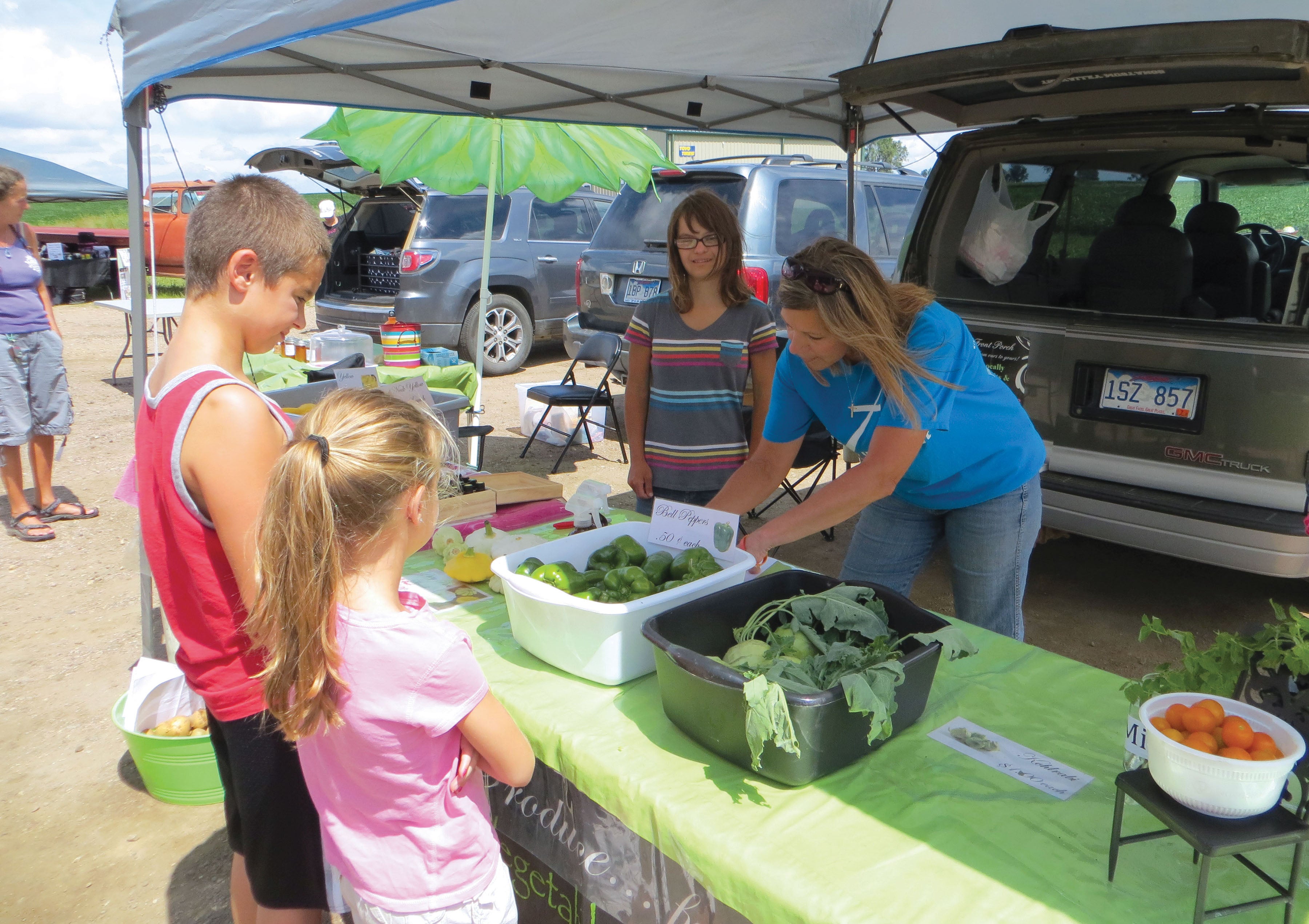 Two female vendors serving a young girl and boy at a vendor stall at a farmers market.
