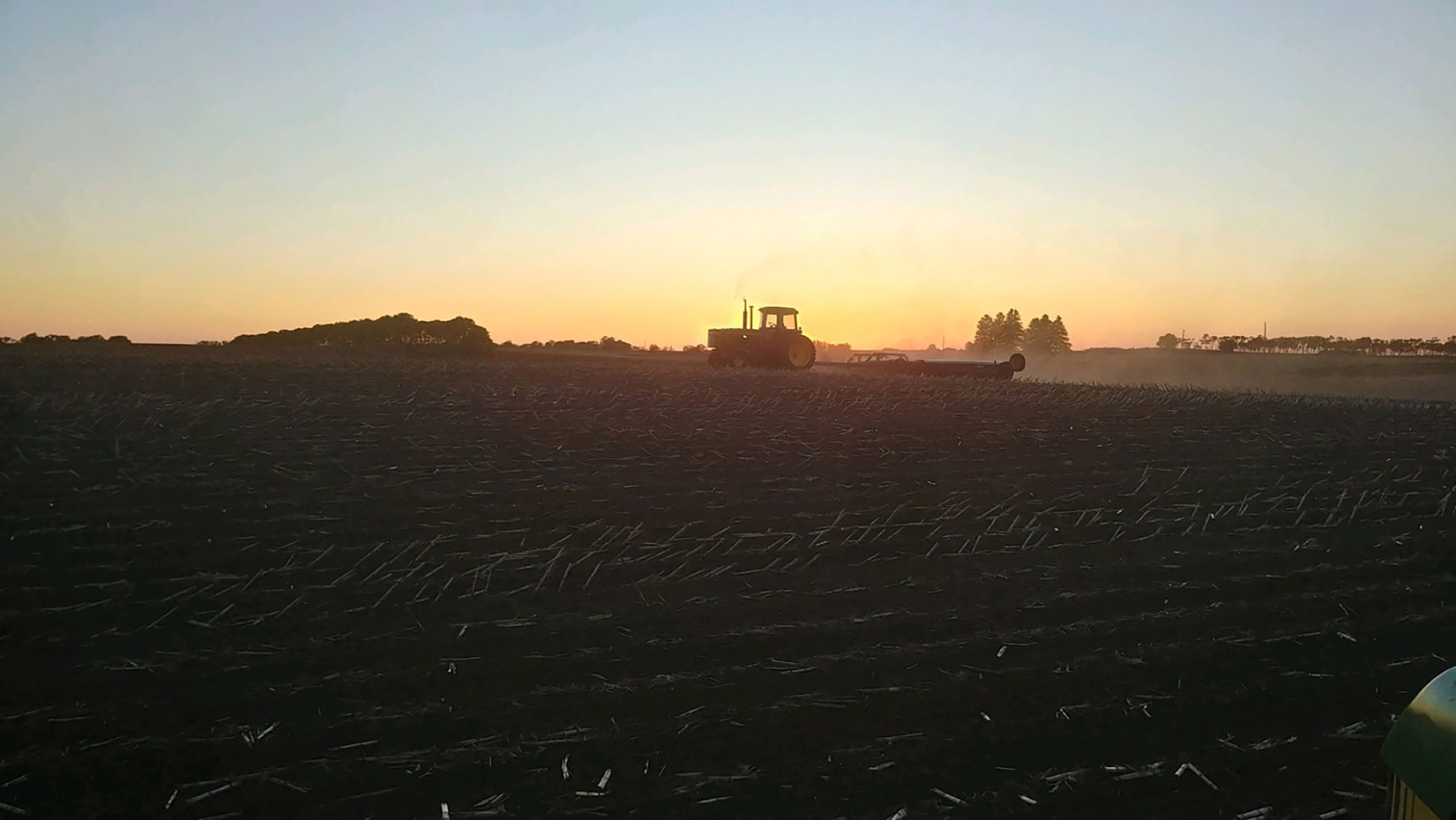 Tractor preparing a soybean field for planting at twilight.
