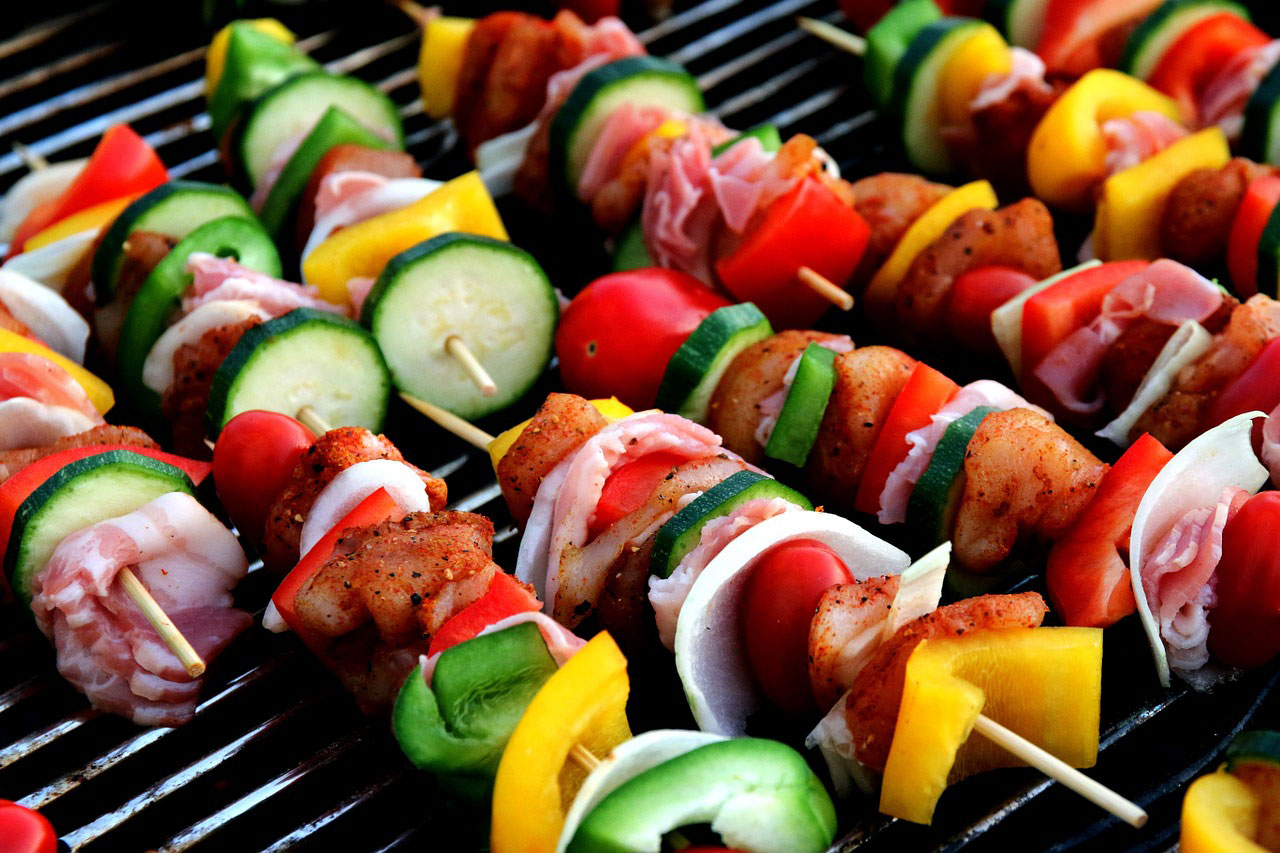 Several kabobs with pieces of fresh vegetables and lean meats cooking on a grill.