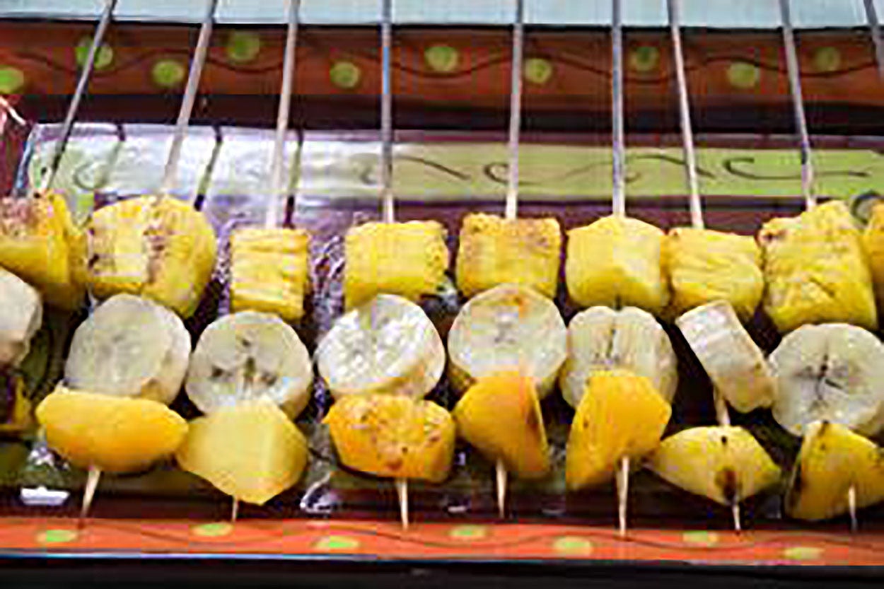 A row of fruit kabobs with pineapple chunks, banana pieces, and peach chunks ready for grilling.