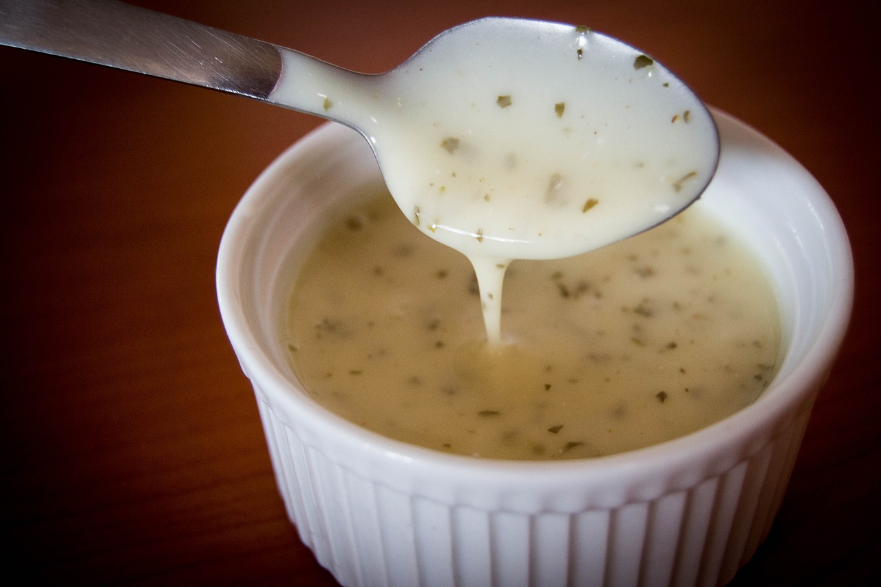 A spoon lifting creamy, white salad dressing from a whit ramekin.