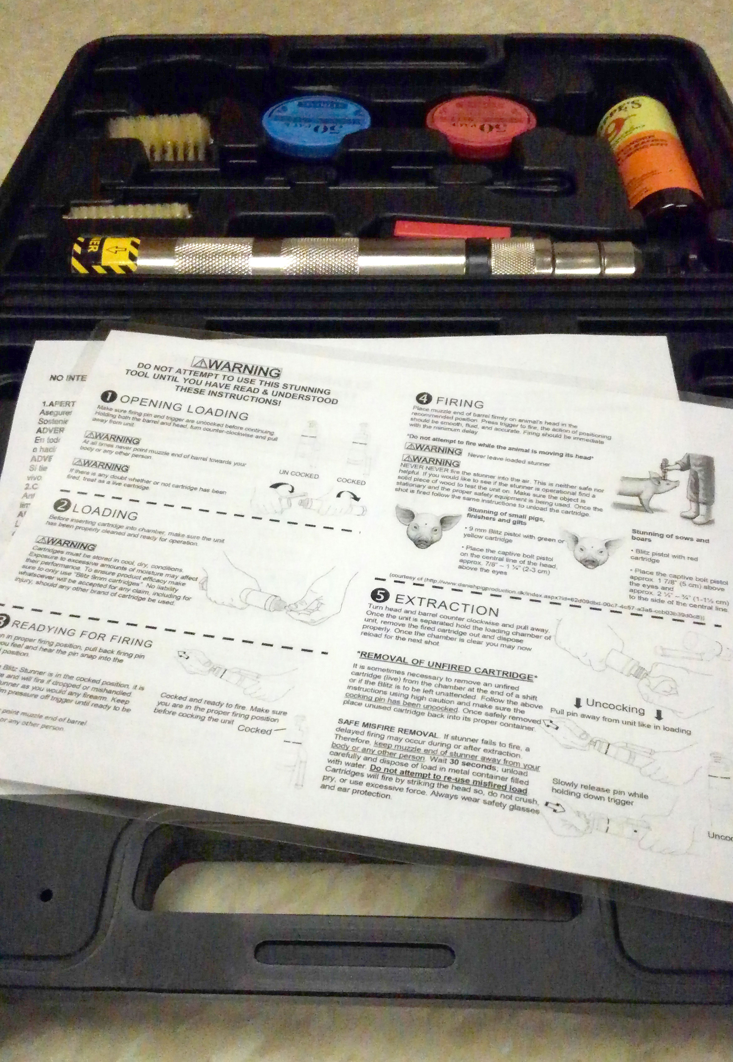 A black, plastic case containing a captive bolt stunner kit along with laminated instructions for properly using the tool for euthanasia.