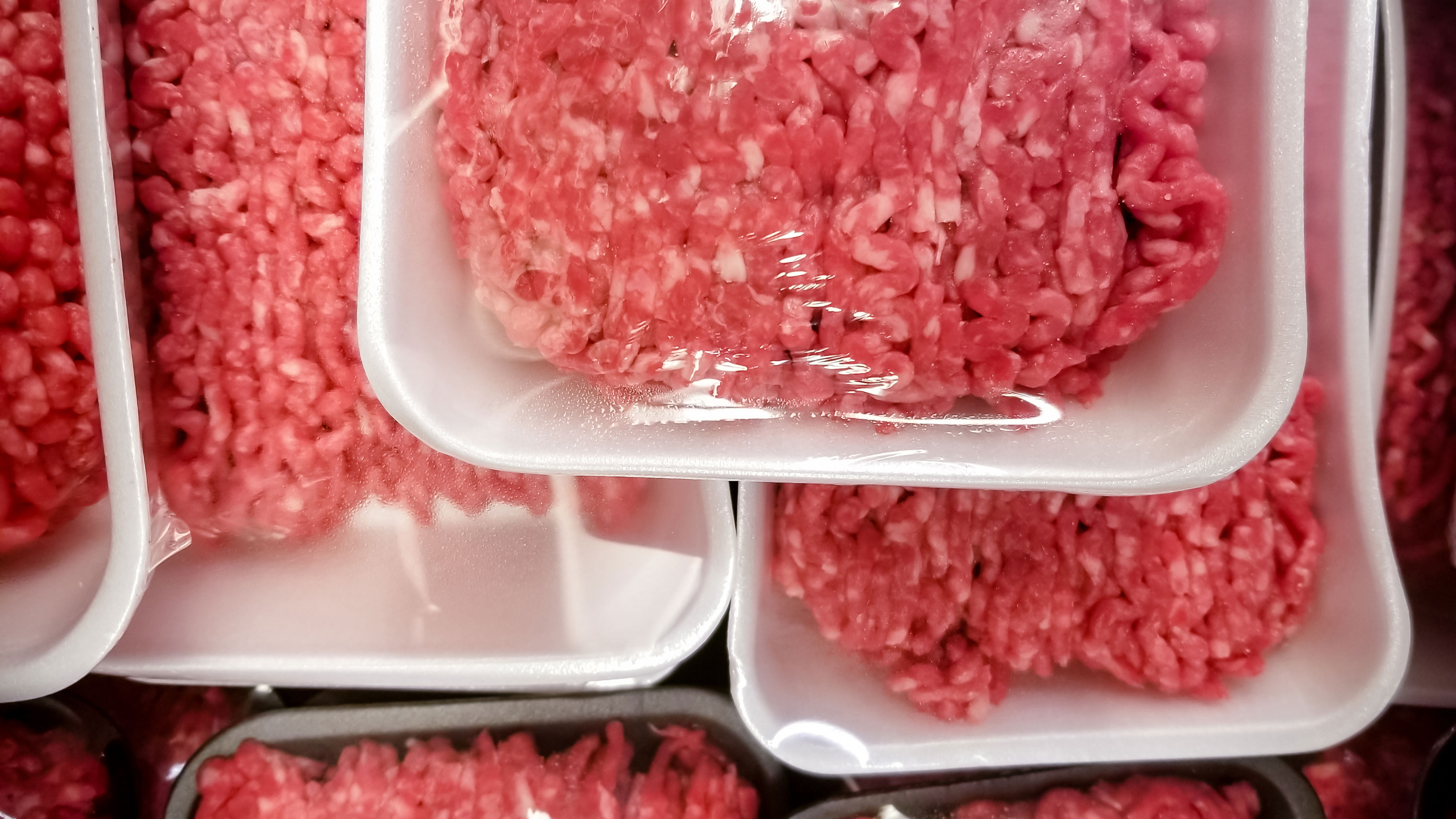 Sealed packages of ground beef stacked inside a meat cooler at a grocery store.