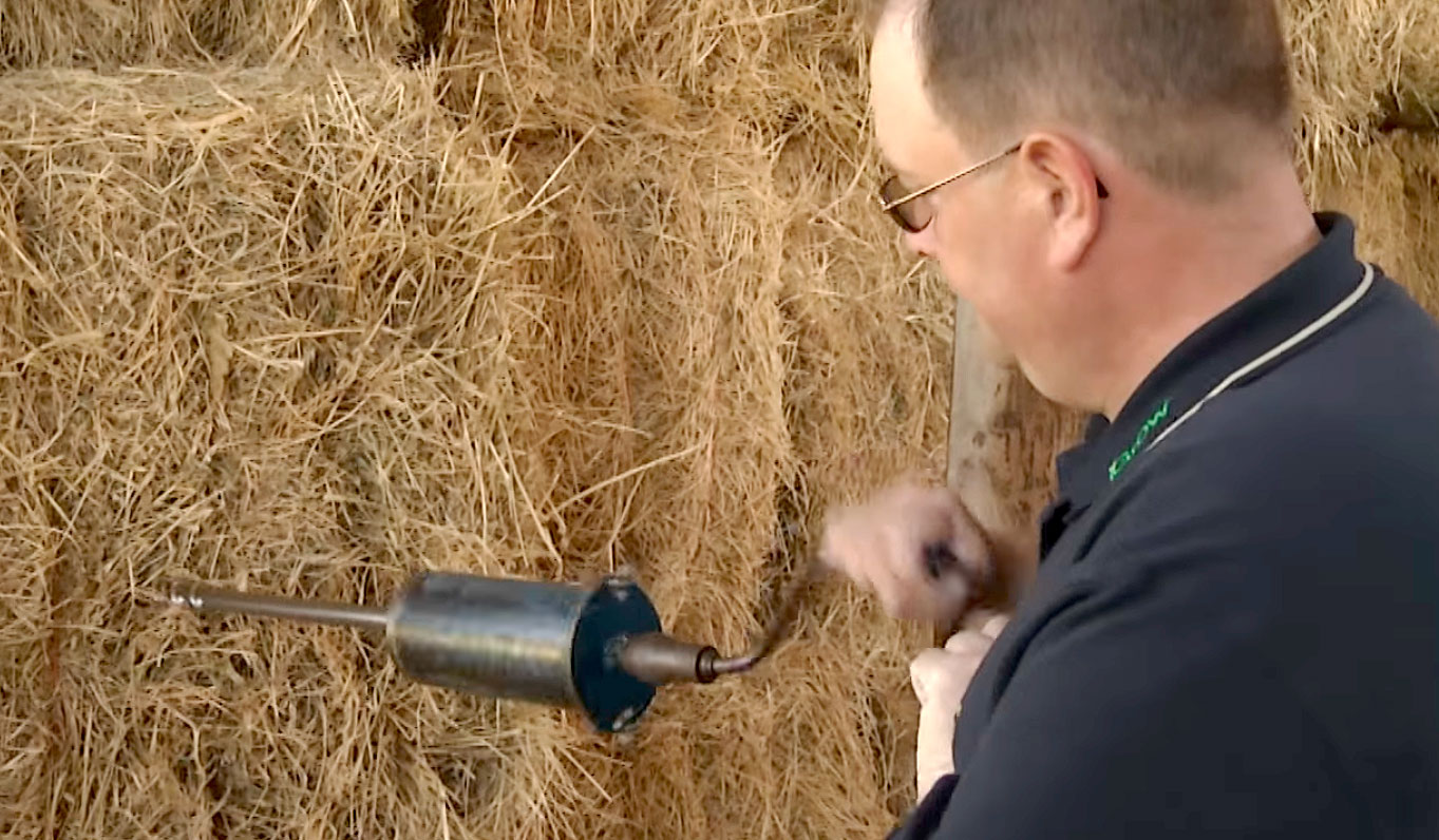 A man drilling a core sampler into the side of a hay bale.