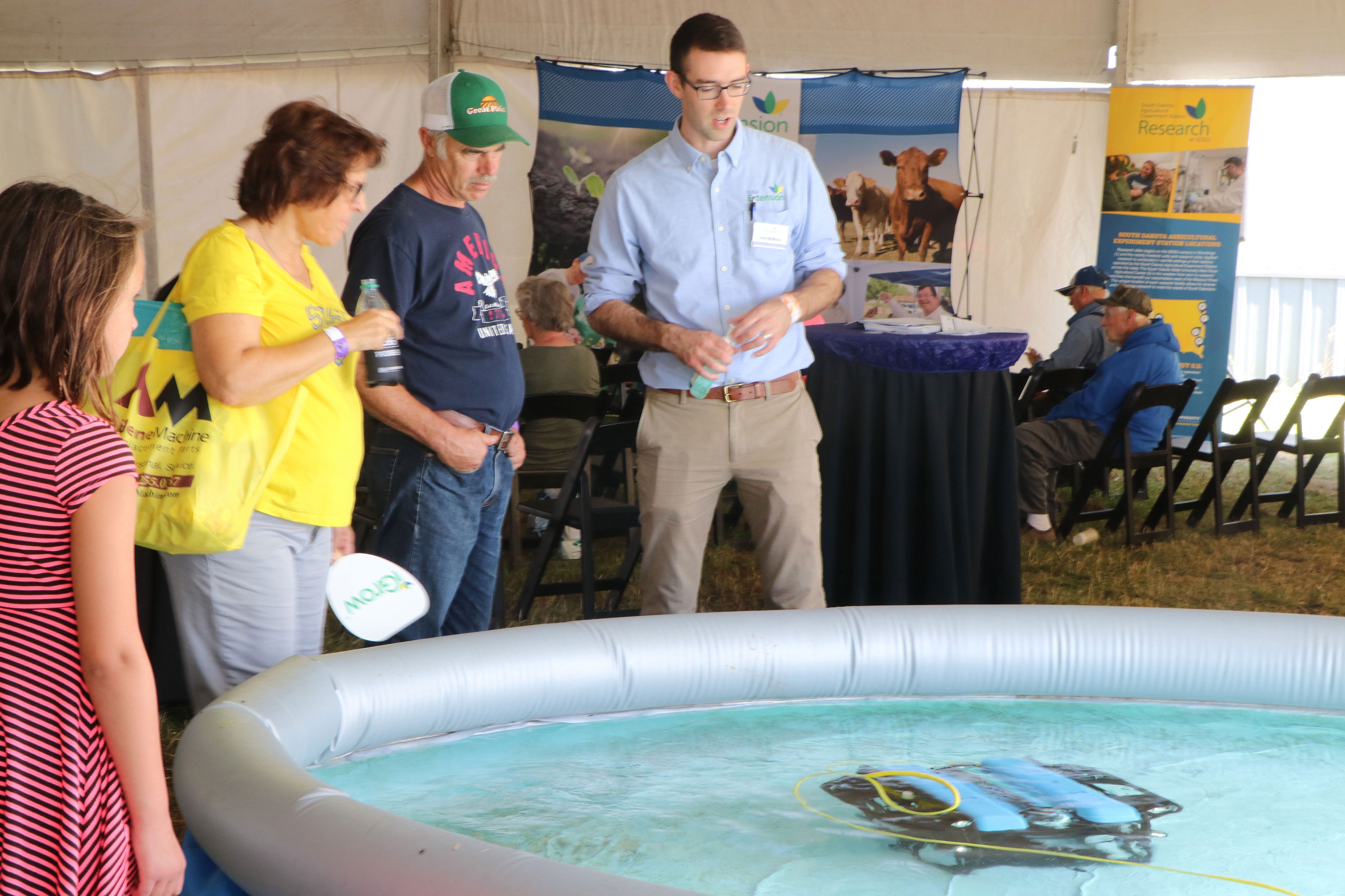 John McMaine, Assistant Professor & SDSU Extension Water Management Engineer, demonstrating an underwater drone in a large pool to a young woman and an older couple.