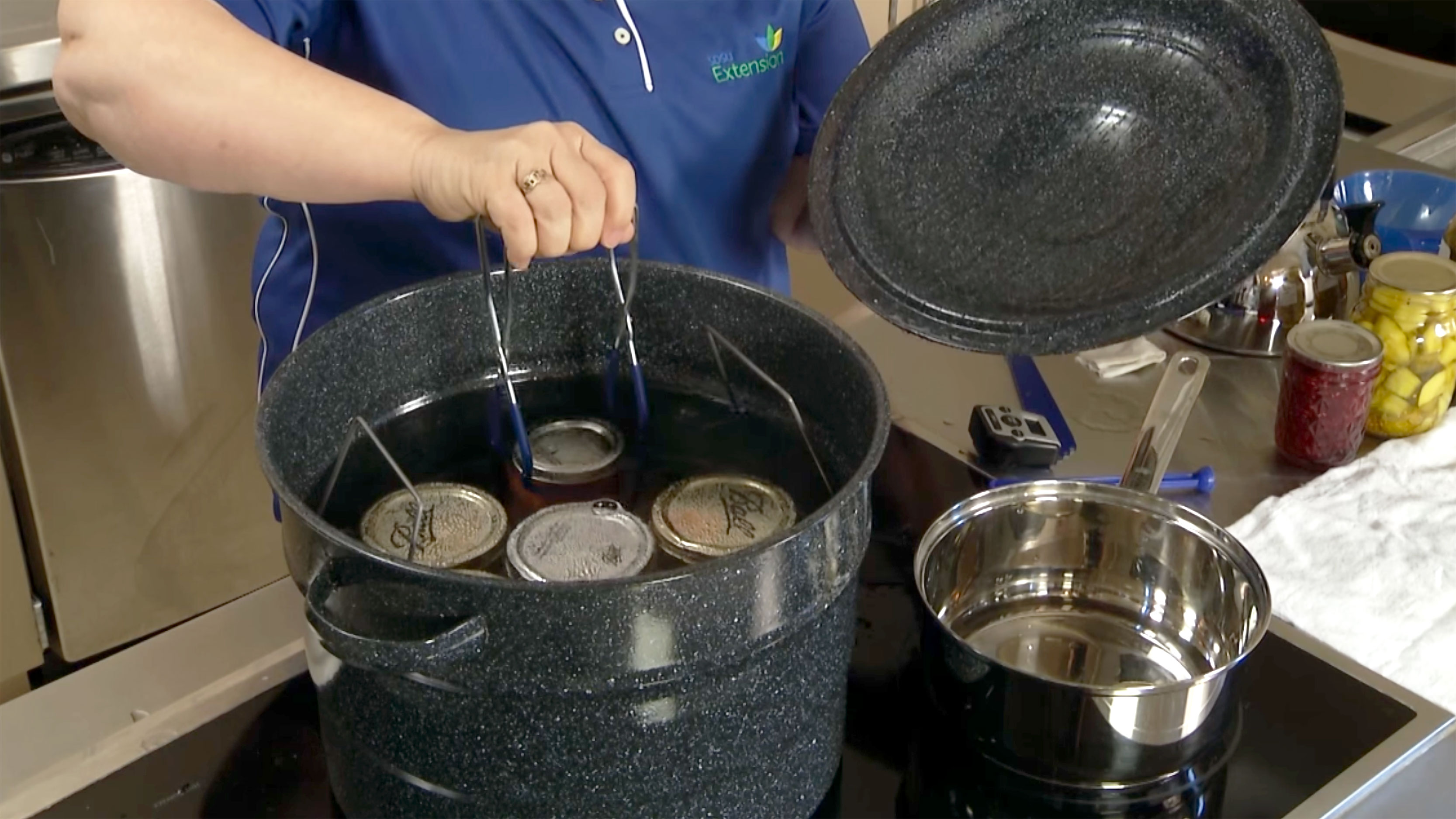 A woman safely placing a can of salsa into a water bath canner.