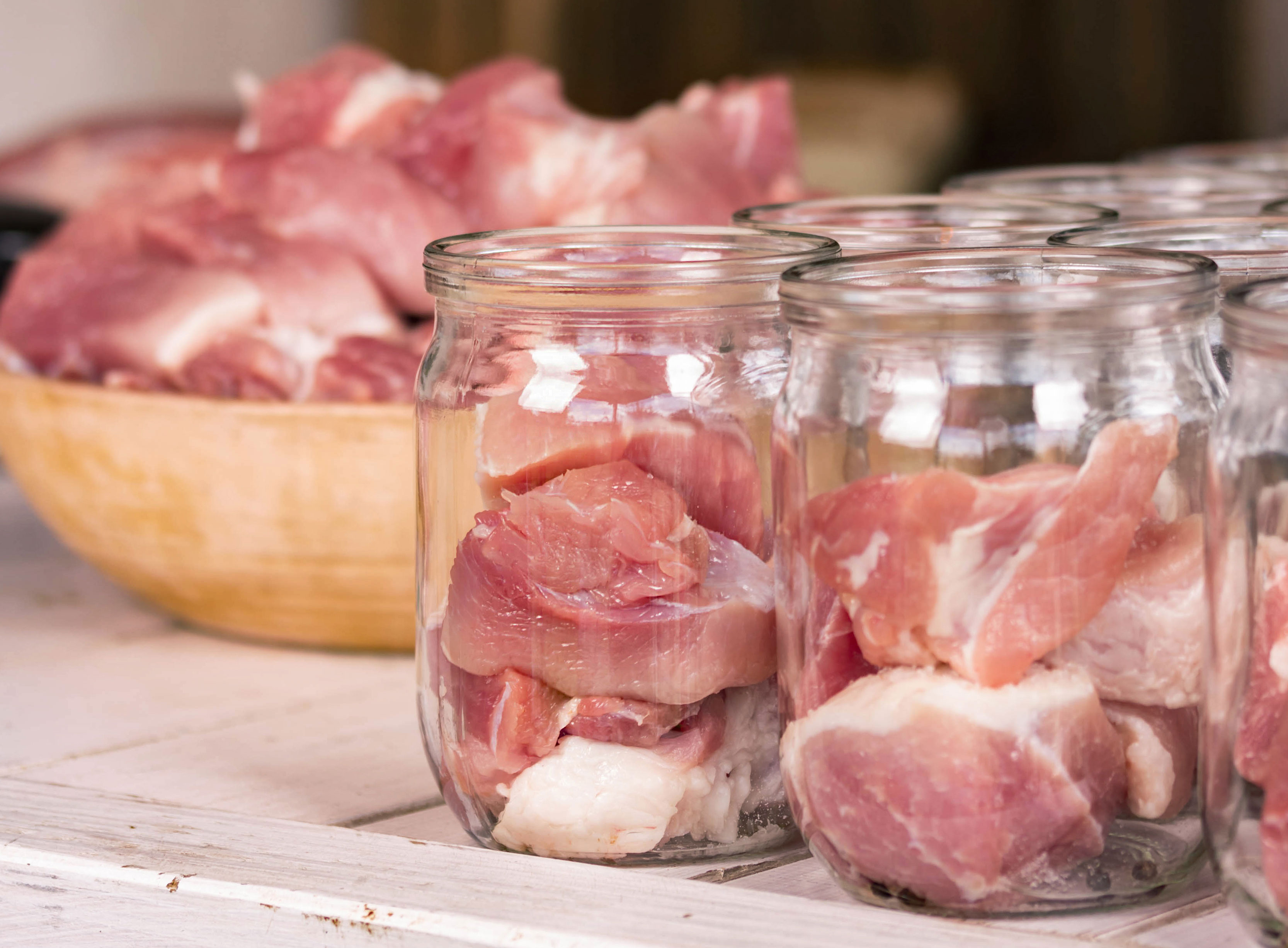A bowl of raw meat being distributed into clear, glass jars.