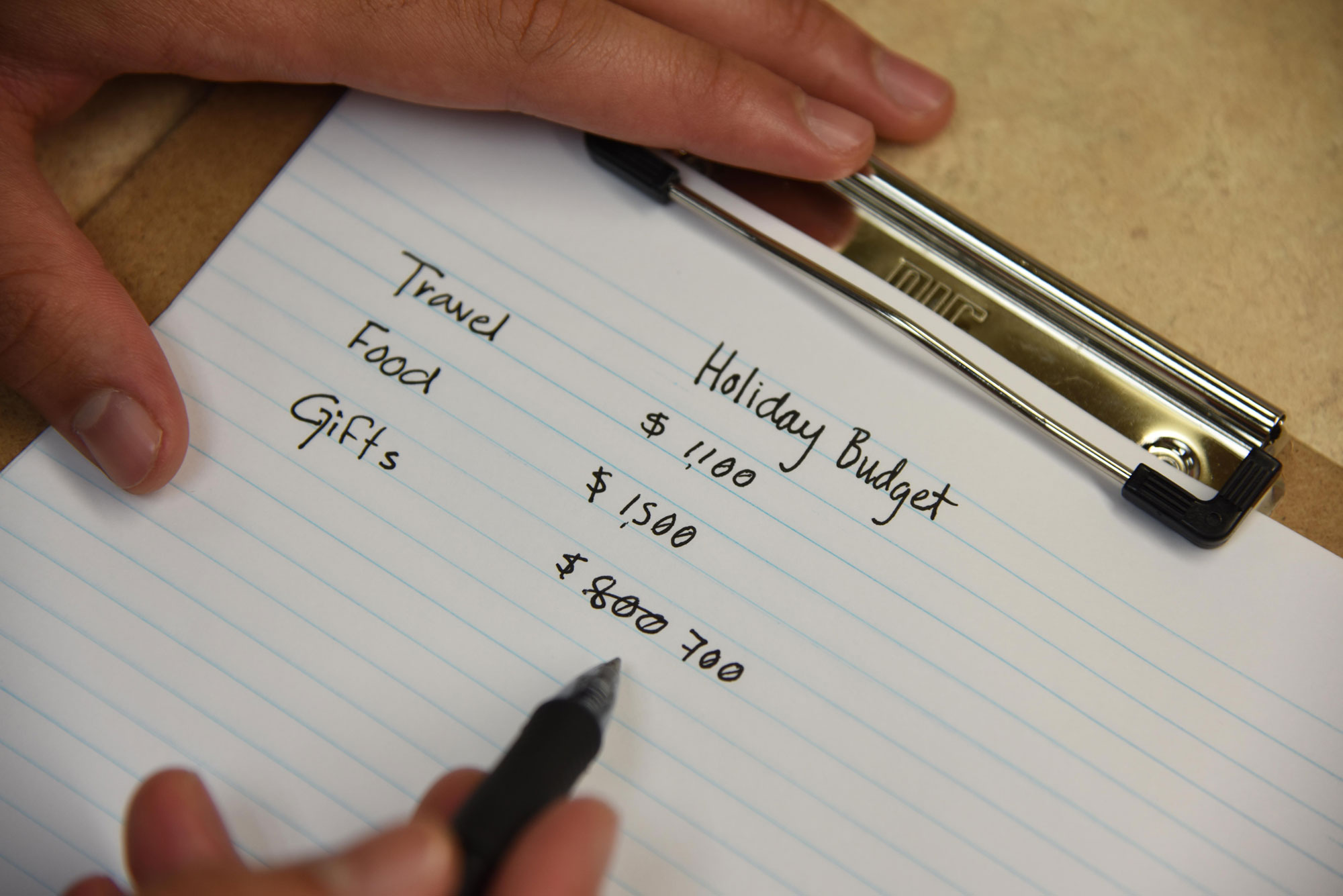 Hands writing out a holiday budget on a notepad.