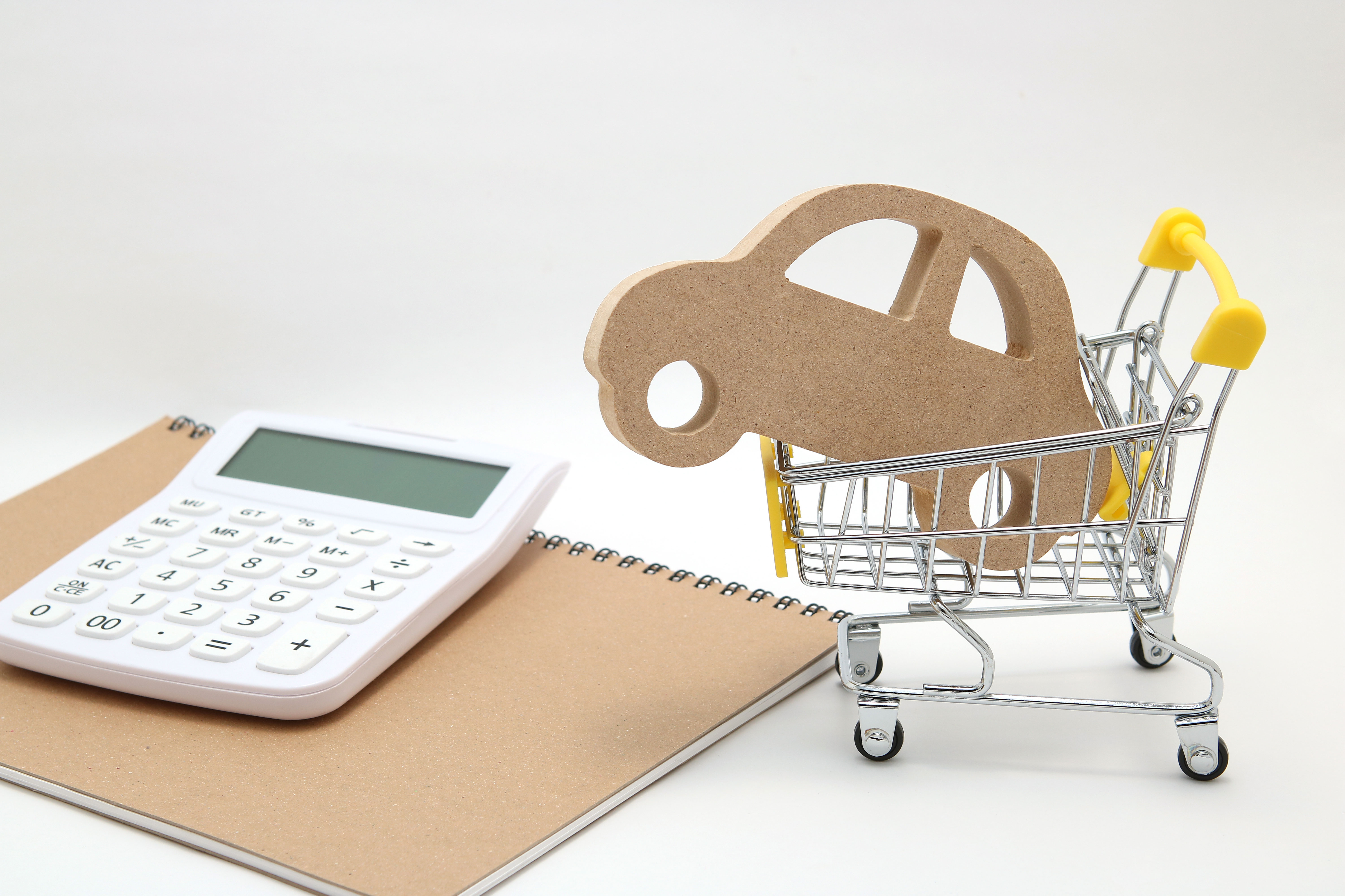 A wooden car cutout placed inside a small shopping cart next to a calculator and a notebook.