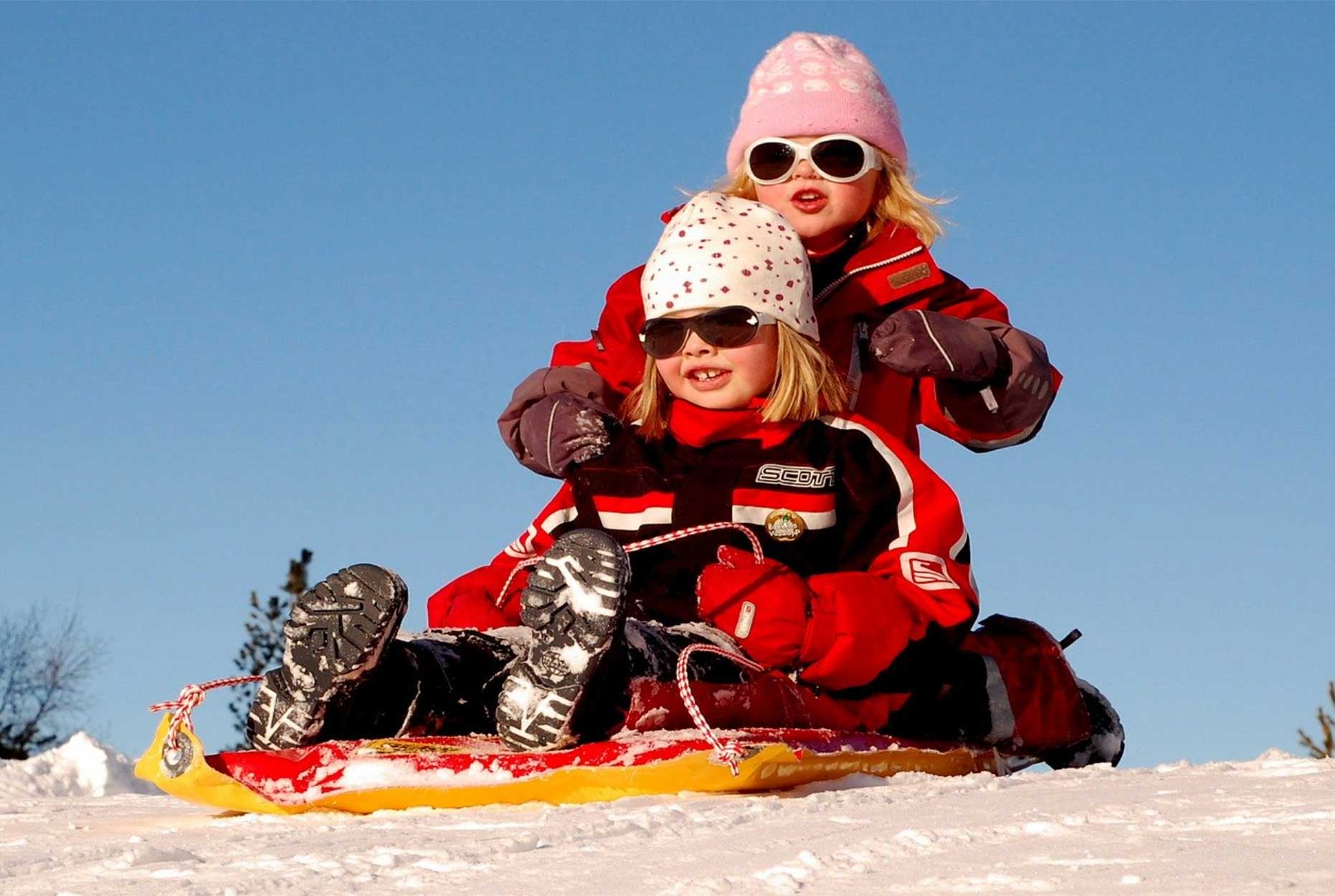 Two young girls in winter clothing riding on a sled.