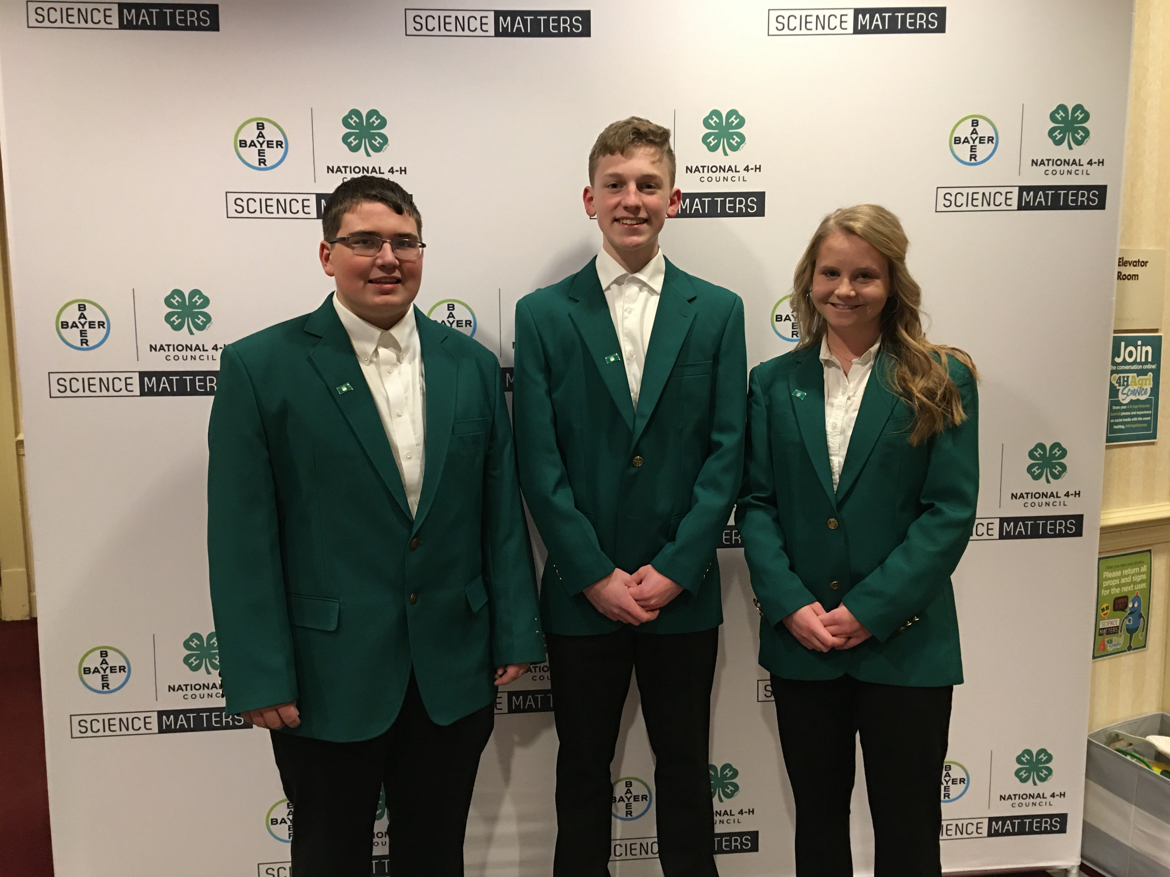 an image of three youth in green jackets in front of a display