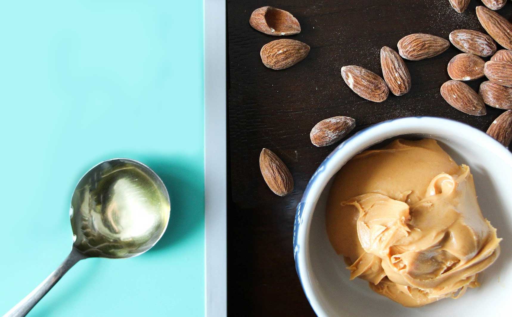 Almonds, a tablespoon of oil, and almond butter sitting on a countertop